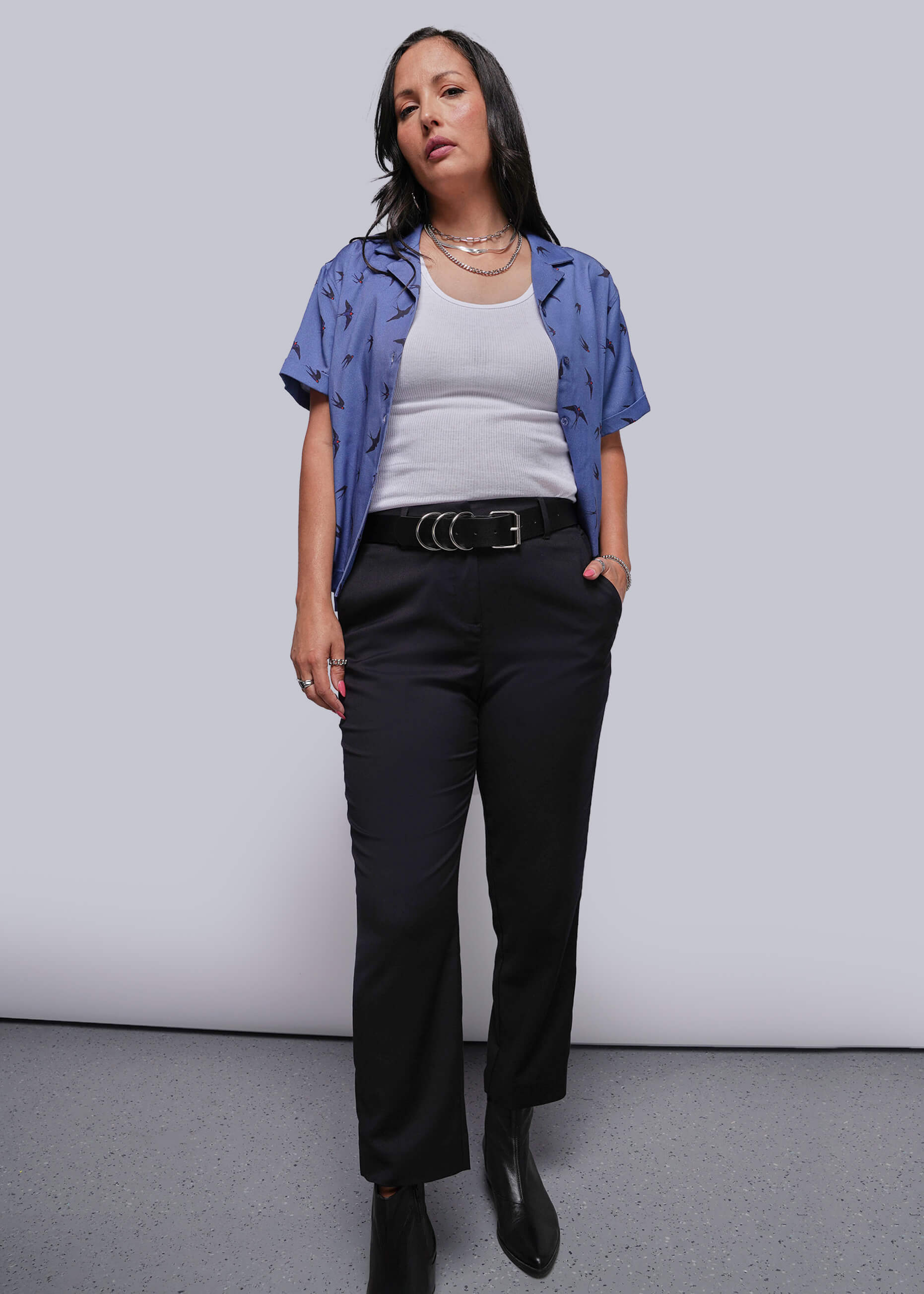 Person wearing a blue shirt, white top, black pants, and black shoes against a plain background