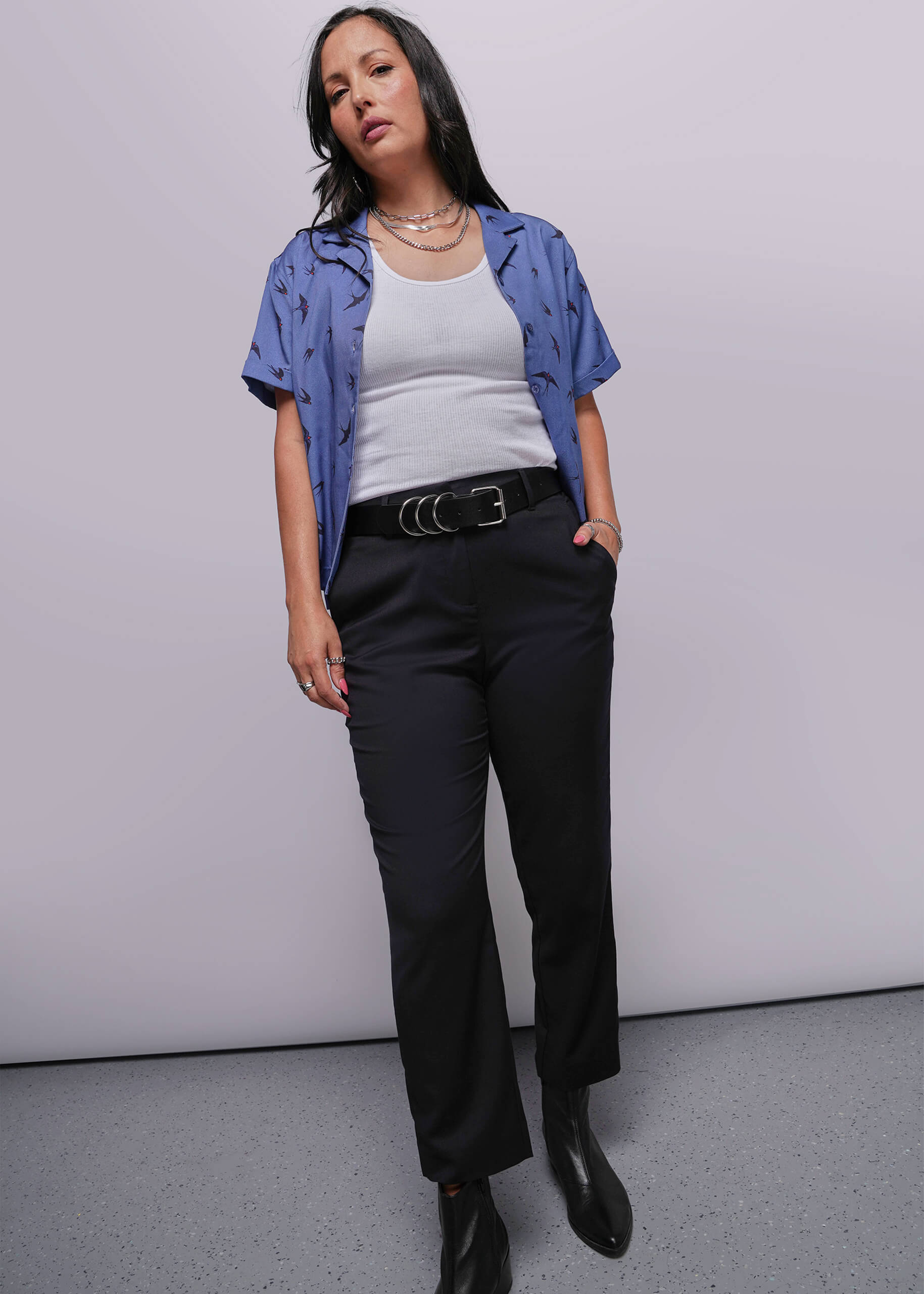 S=Person wearing a blue shirt, white top, black pants, and black shoes against a plain background