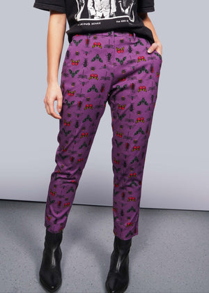 S= Pictured from the waist down, model stands in front of white studio backdrop wearing black graphic tee, black boots, and The Empower Slim Crop Pant in Insect Grape, a purple fabric with colorful insects printed on it.