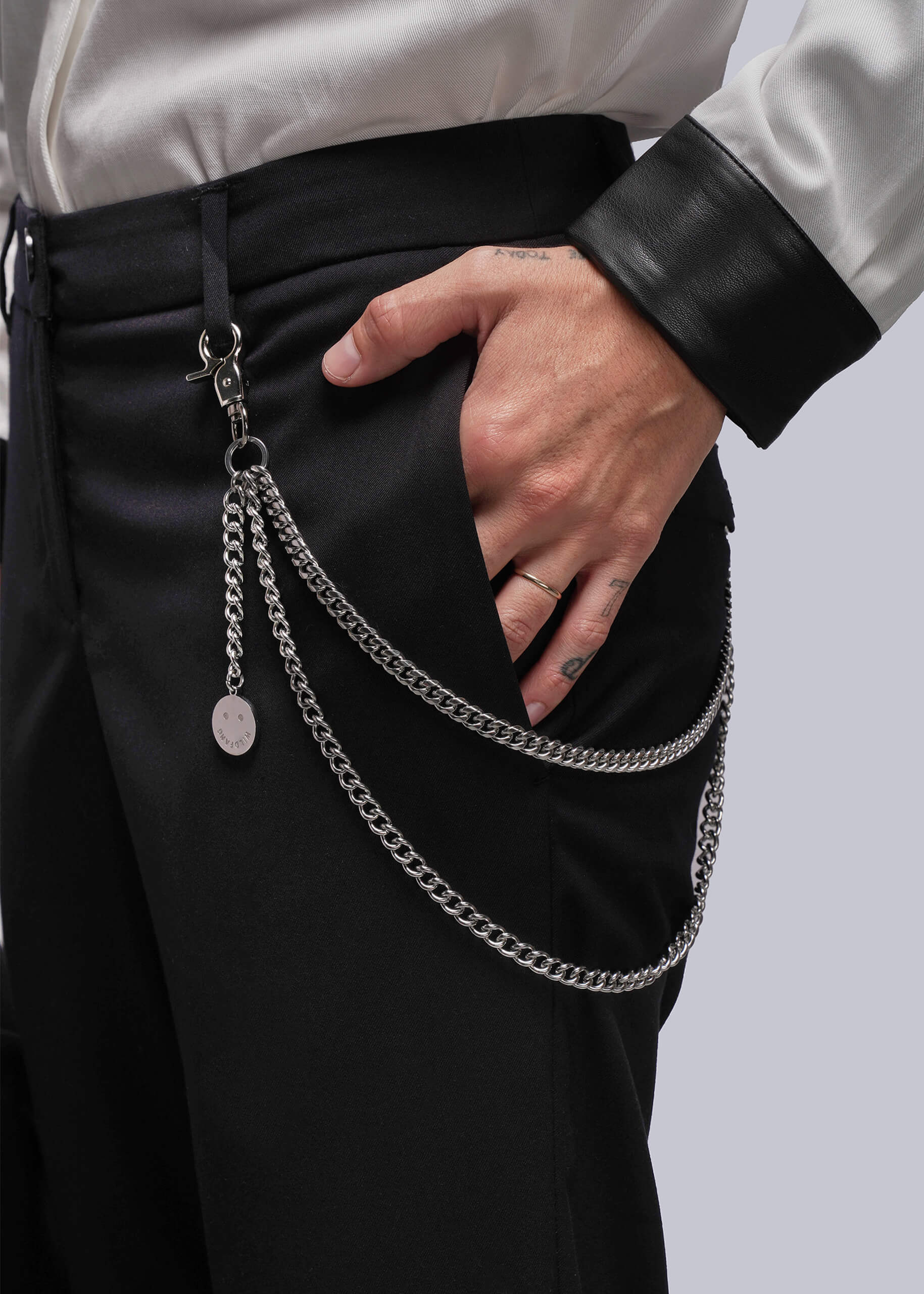S=Person wearing a silver chain accessory on black pants against a neutral background