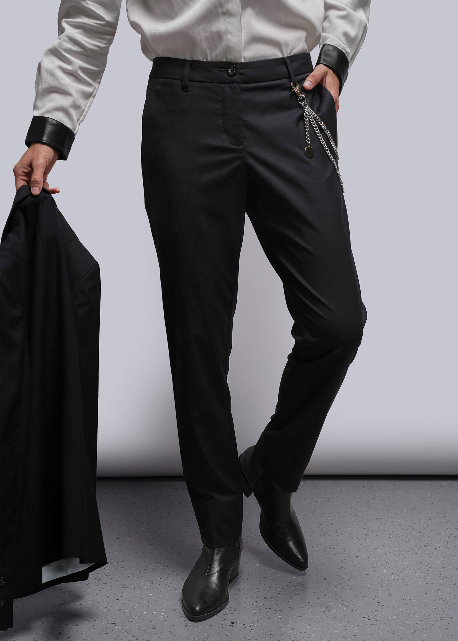 From waist down person wearing black pants and holding a black jacket against a white background
