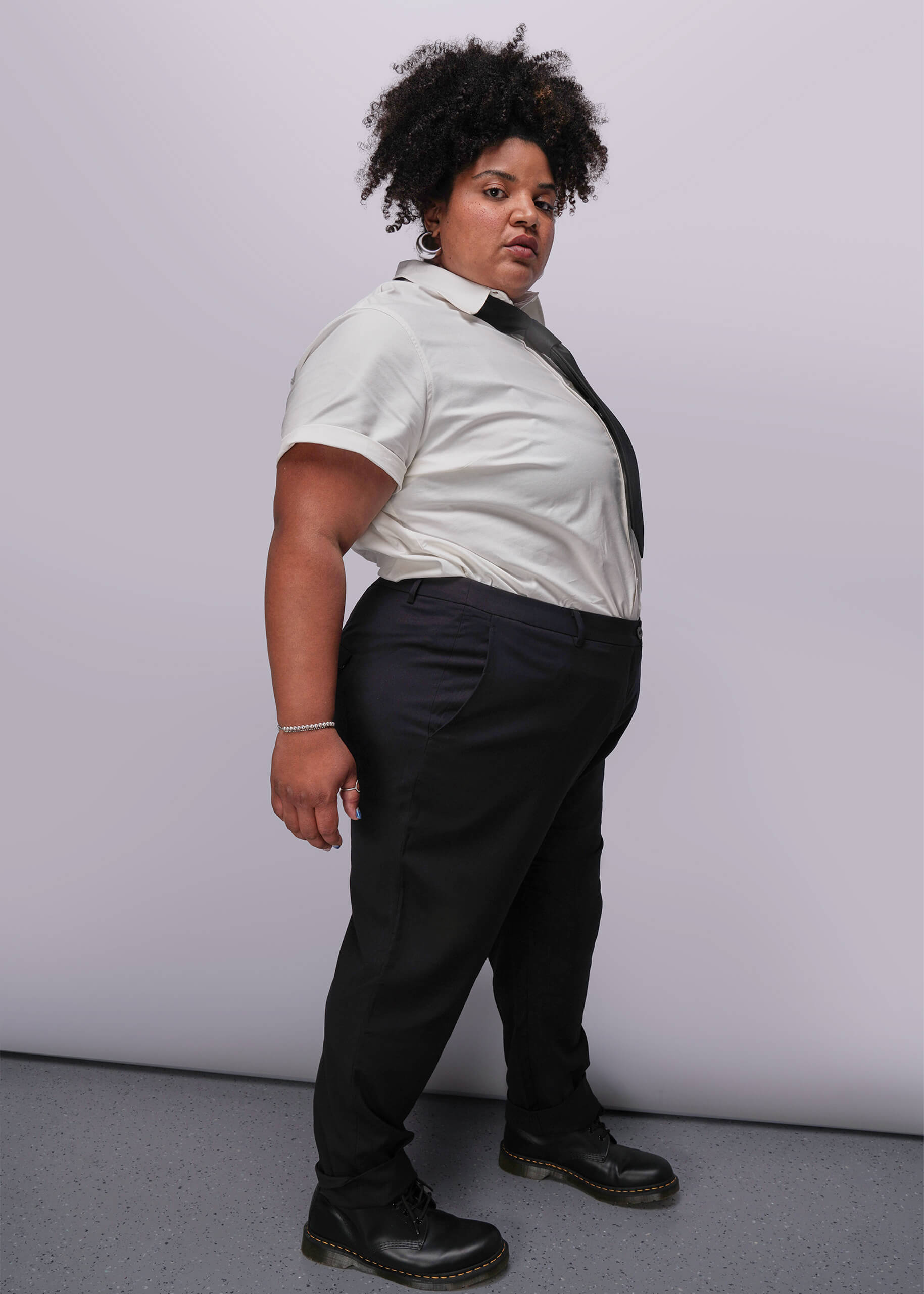 1X=Person wearing a white shirt, black tie, and black pants against a plain background