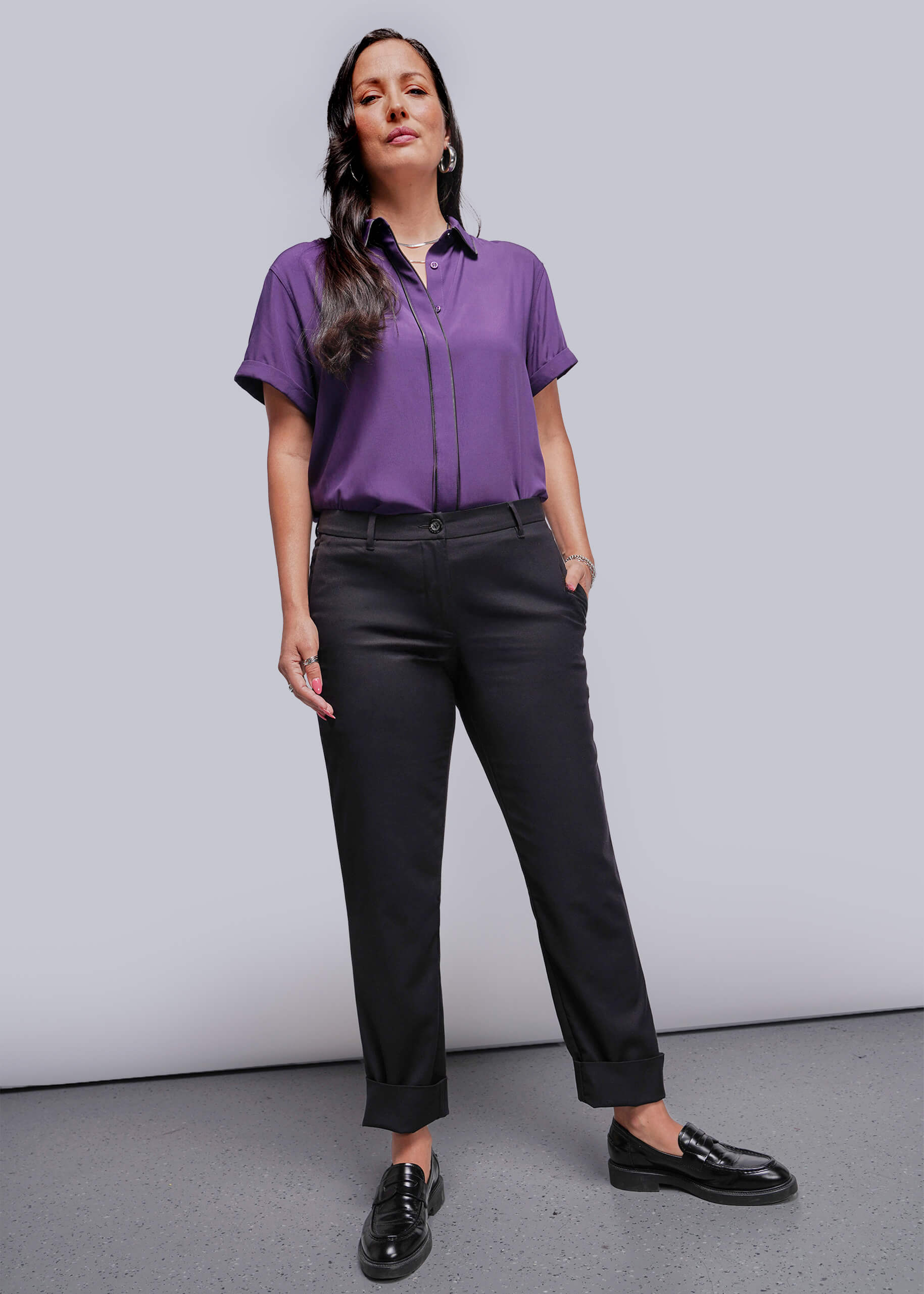 Woman wearing a purple shirt and black pants against a plain background
