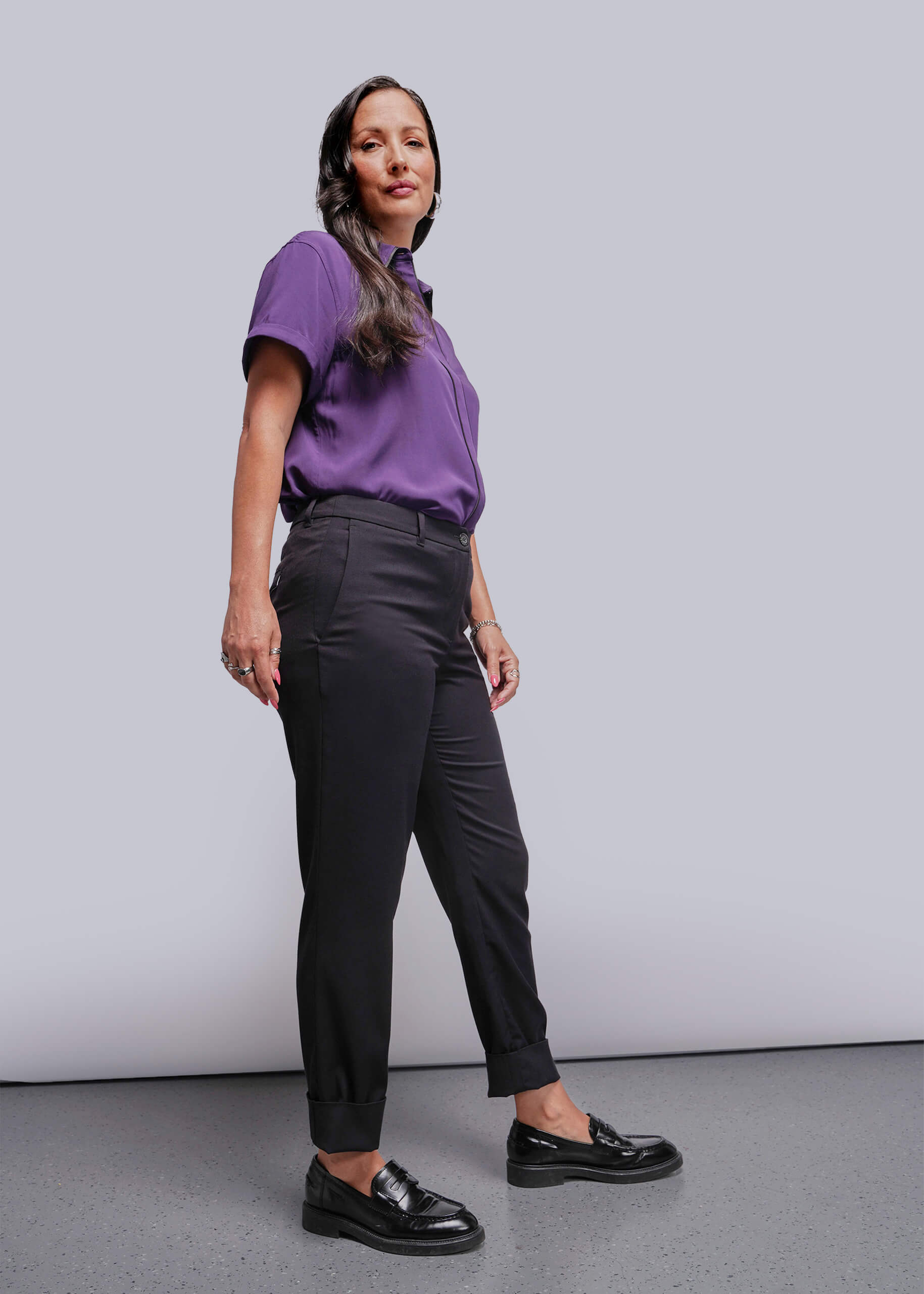 S=Woman wearing a purple shirt and black pants against a plain background