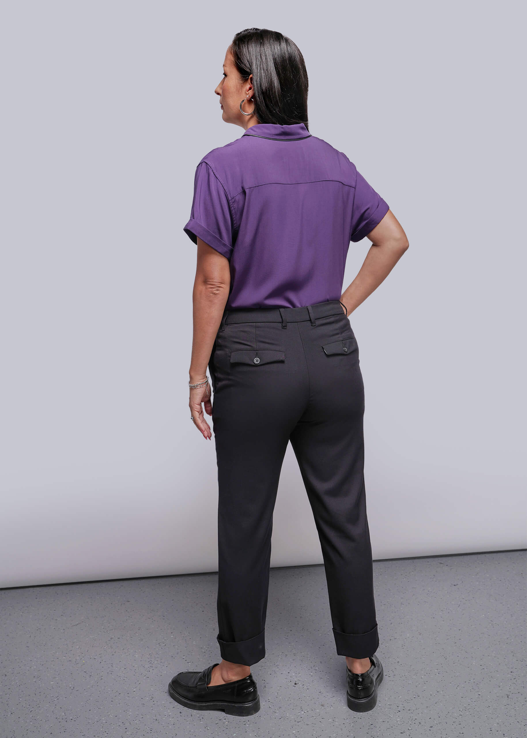 S=Person wearing a purple shirt and black pants against a plain background