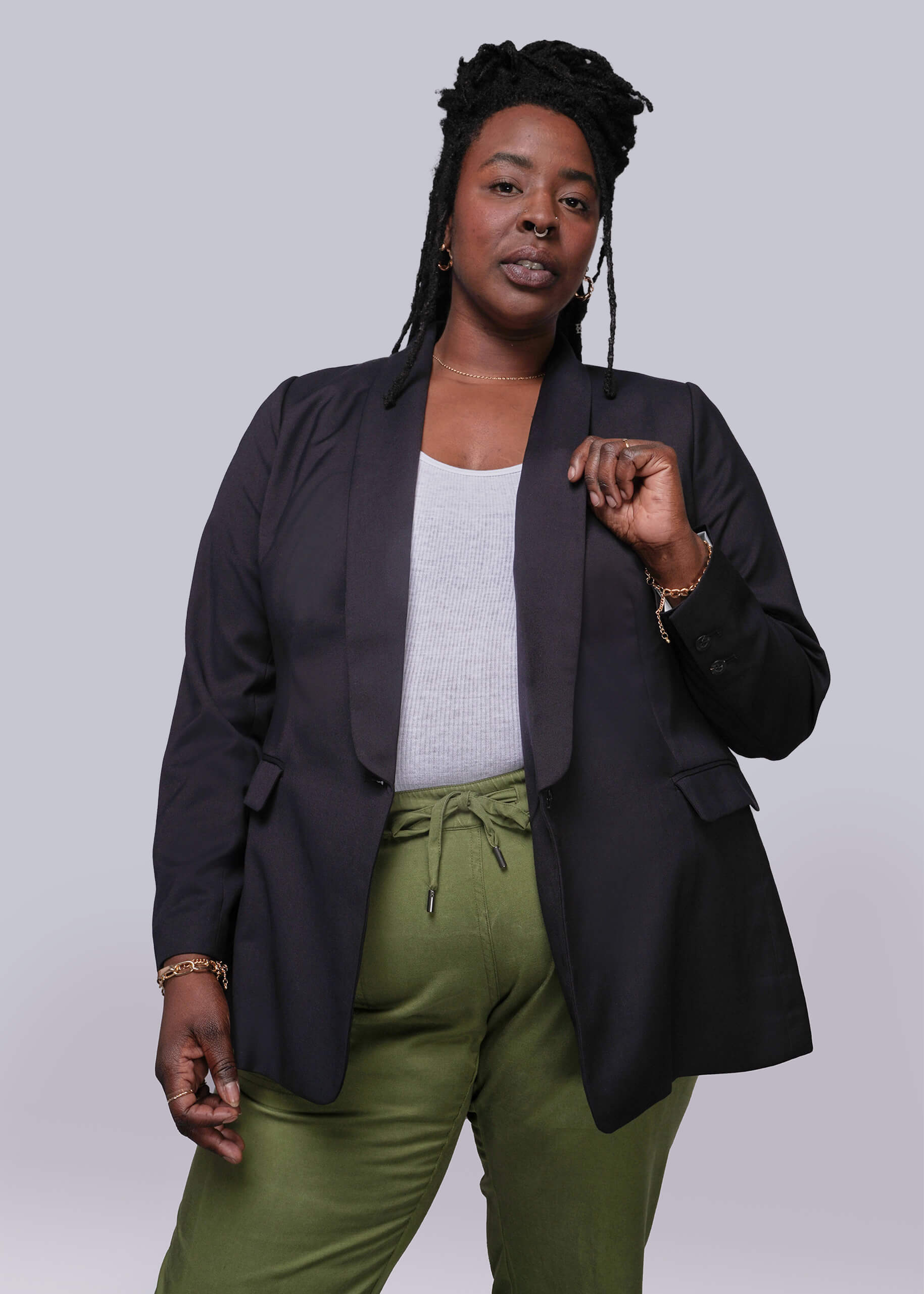 1X=Person wearing a black blazer and green pants against a plain background