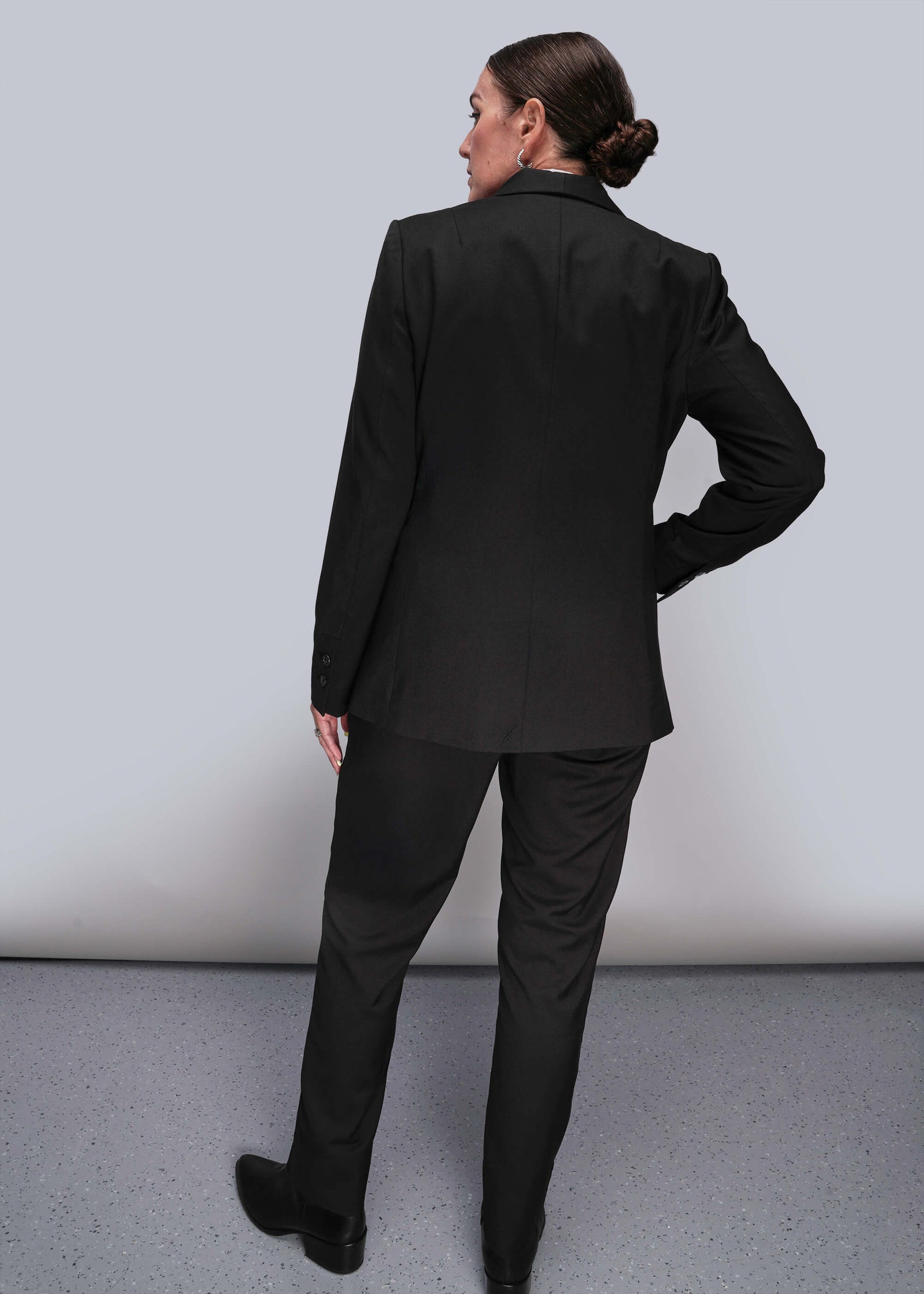 S=Back of person wearing a black suit standing against a plain background