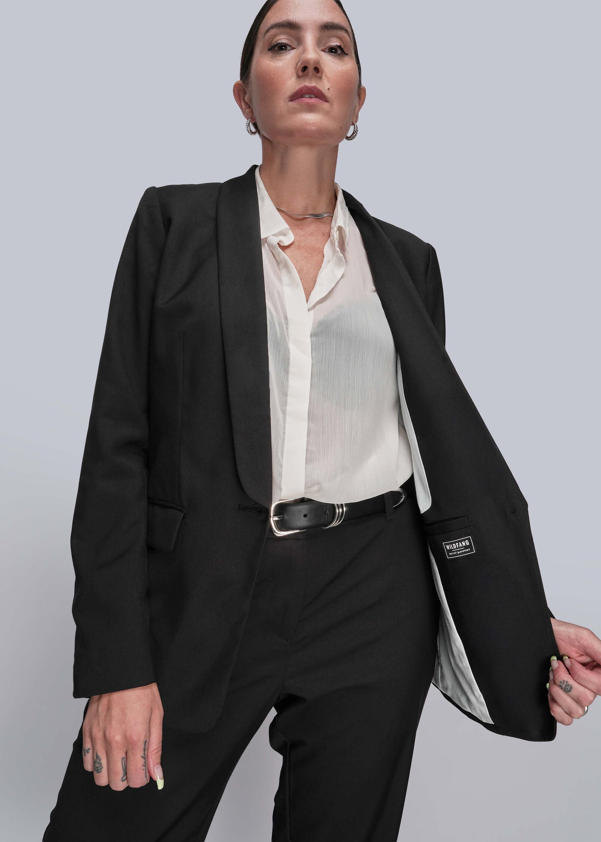 S=Person wearing a black suit with a white shirt on a gray background