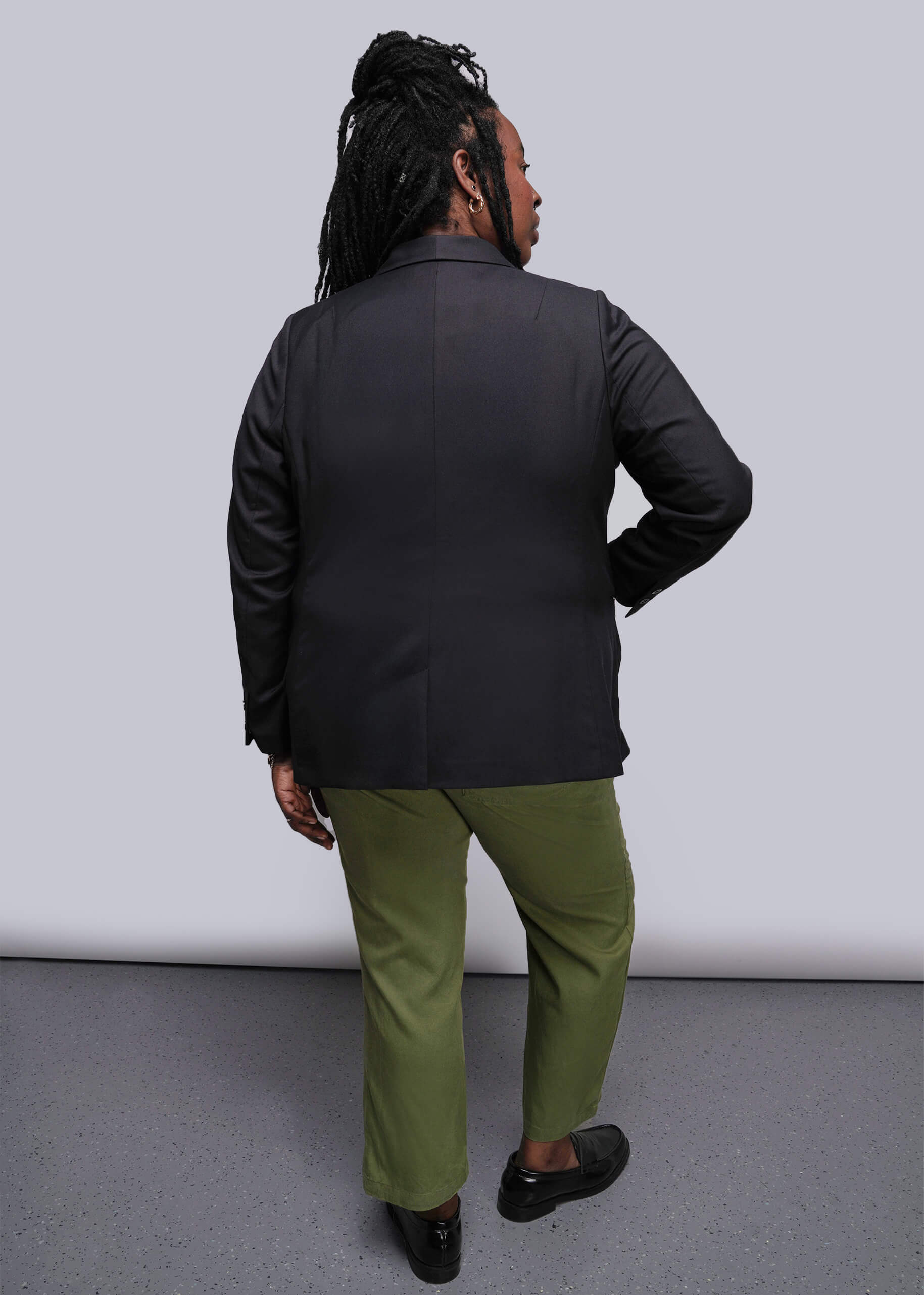 1X=Person wearing a black jacket and green pants standing against a white background