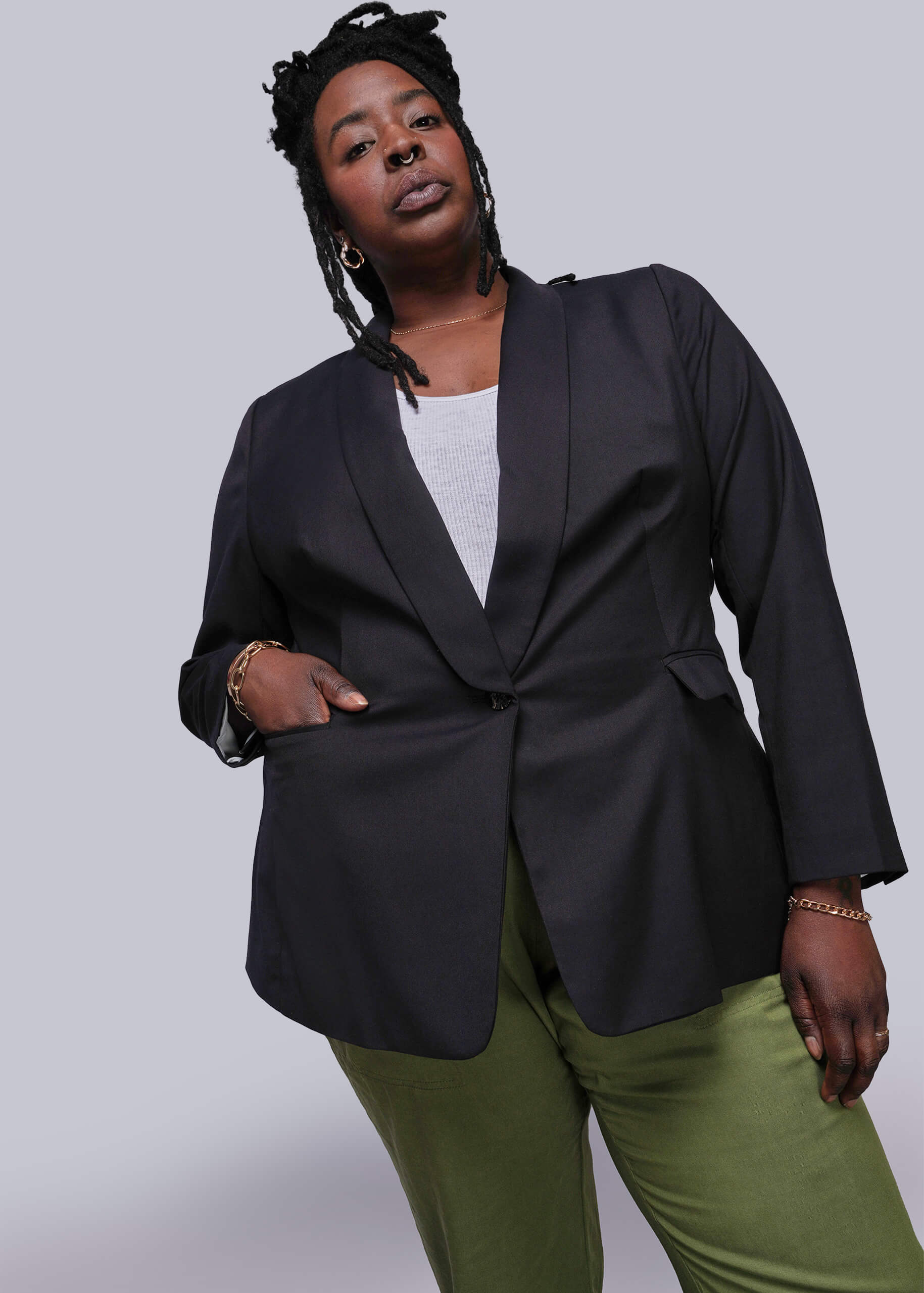 1X=Person wearing a black blazer and green pants against a gray background