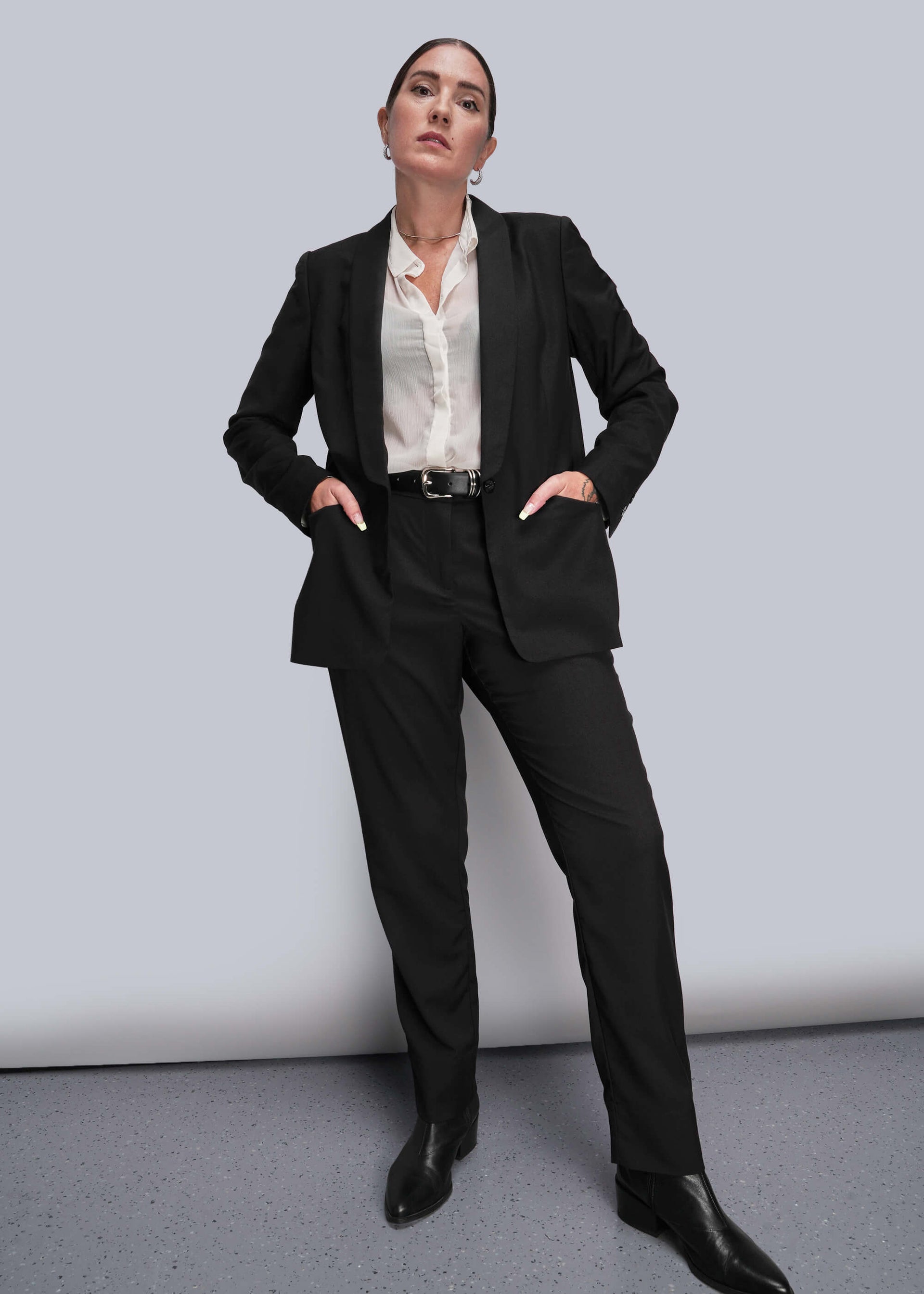 S=Person wearing a black suit with a white shirt on a gray background