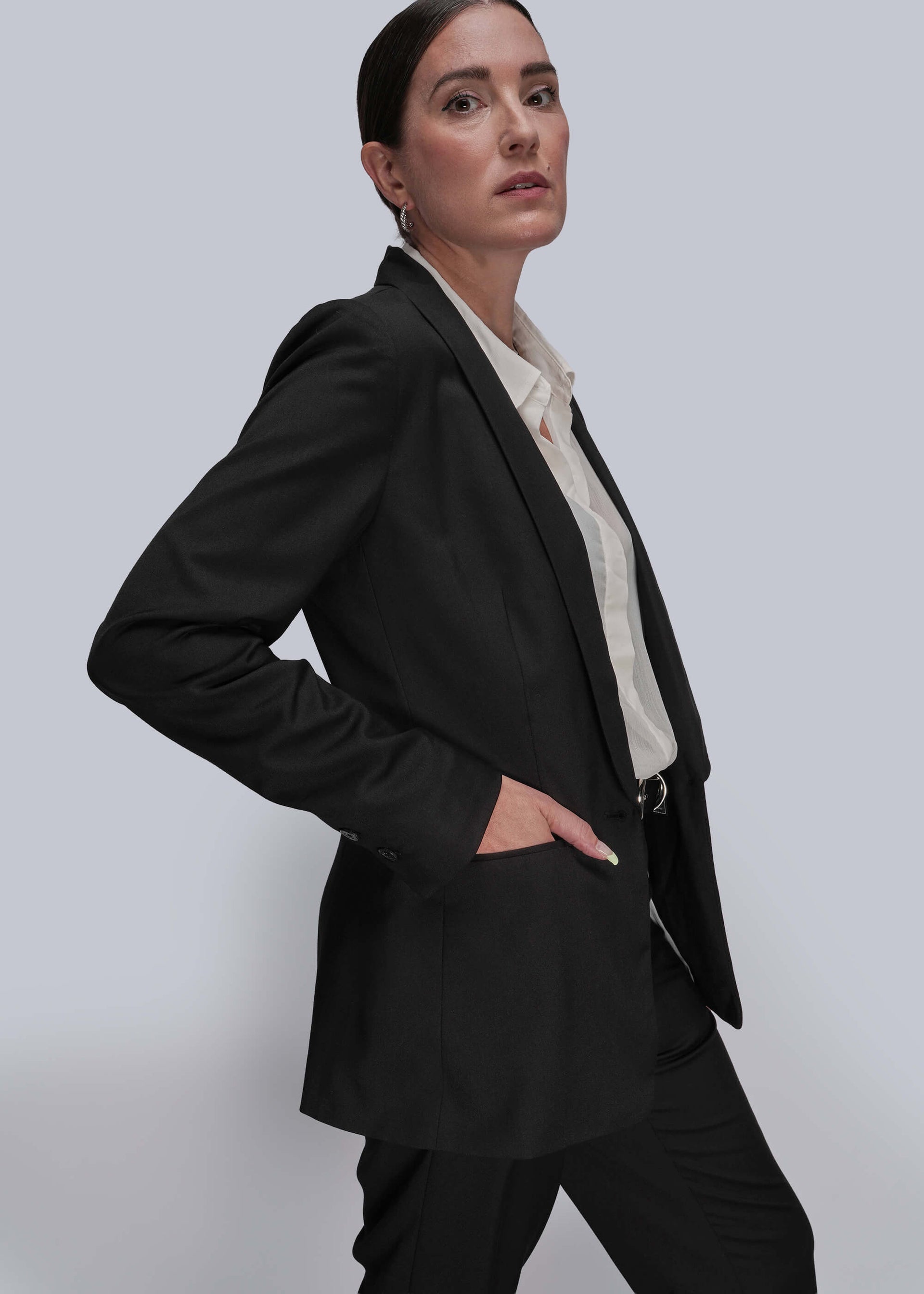 S=Side view of person wearing a black suit with a white shirt on a light gray background