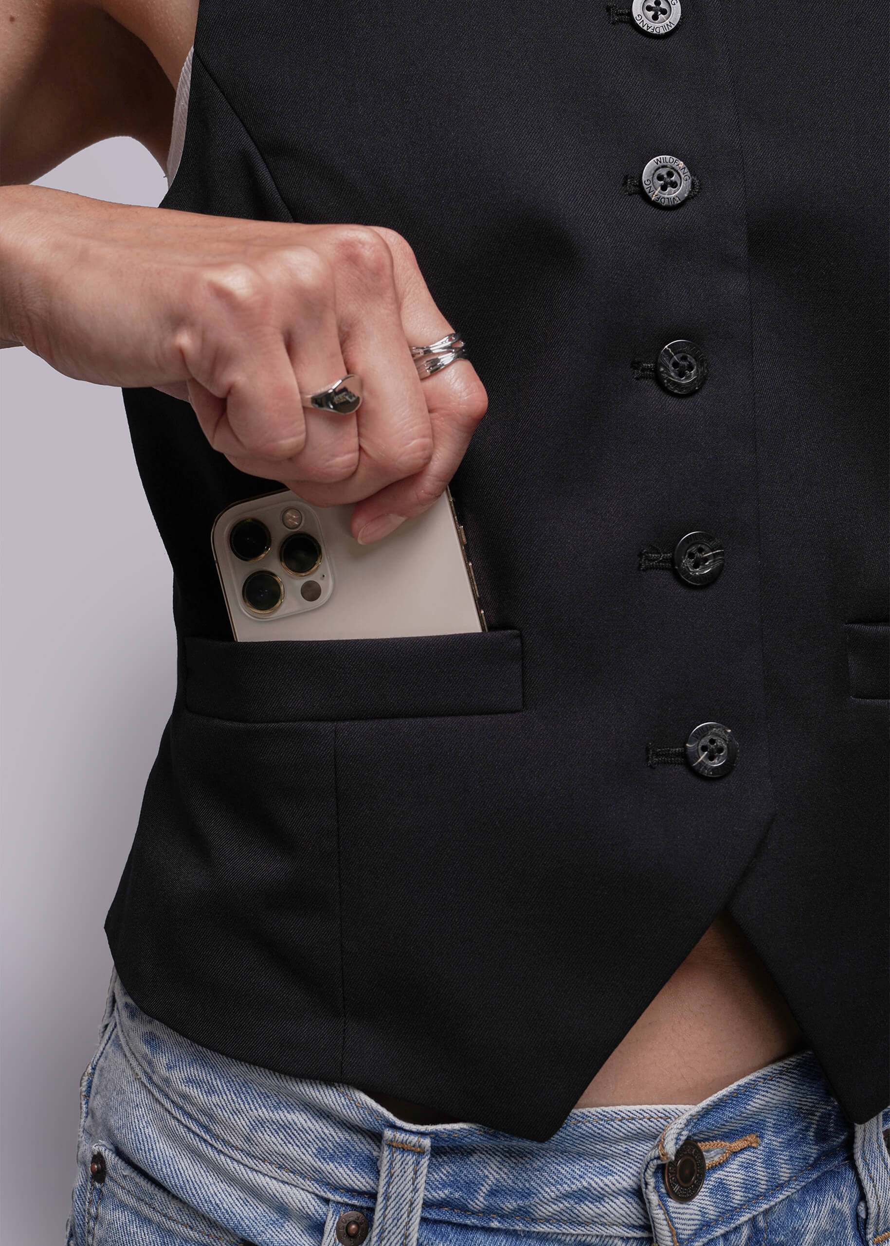 S=Person wearing a black button-up vest with a phone in the pocket against a white background