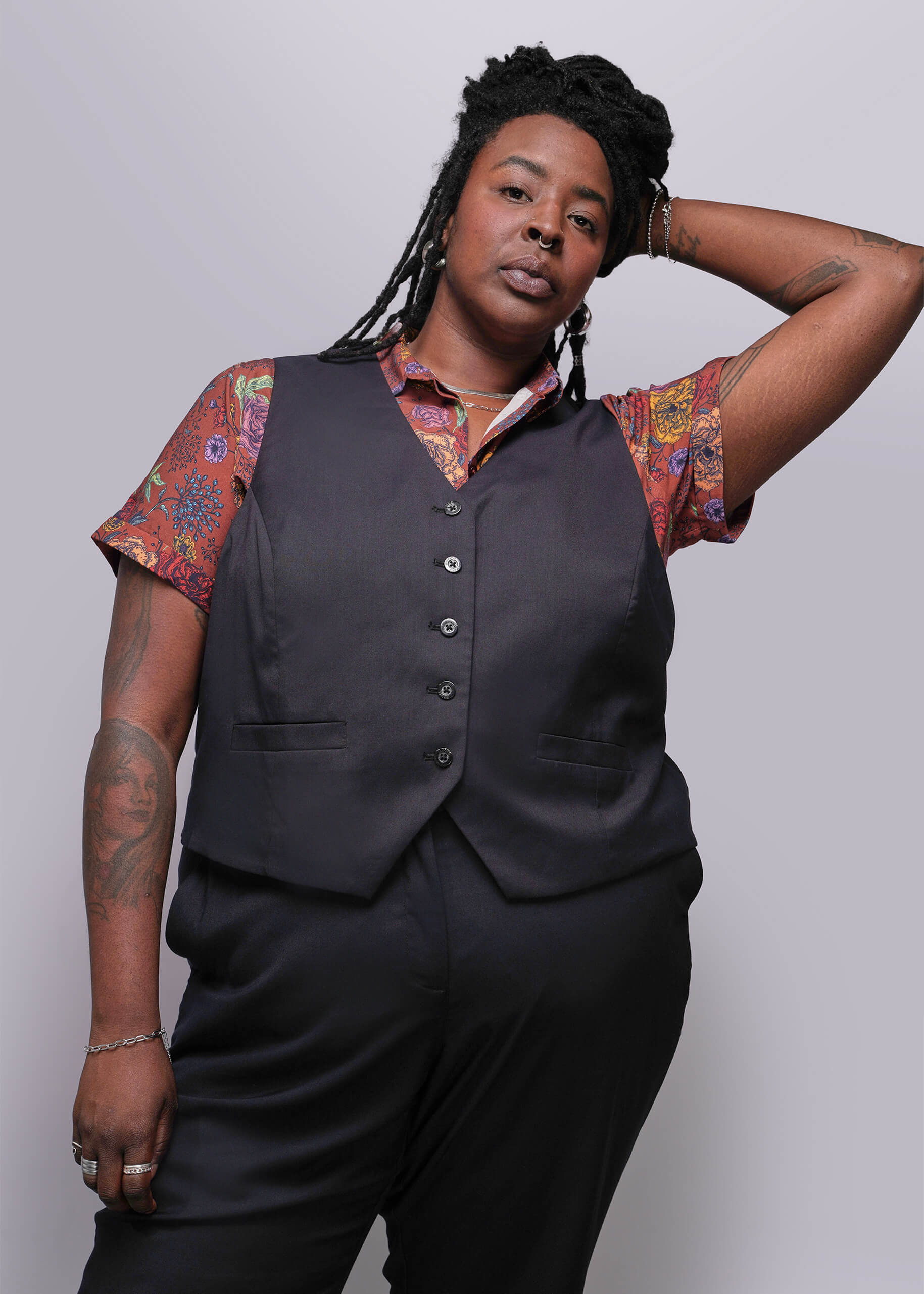 S=Person wearing a black vest over a patterned shirt with a plain background