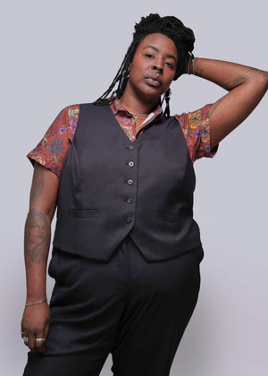 S=Person wearing a black vest over a patterned shirt with a plain background