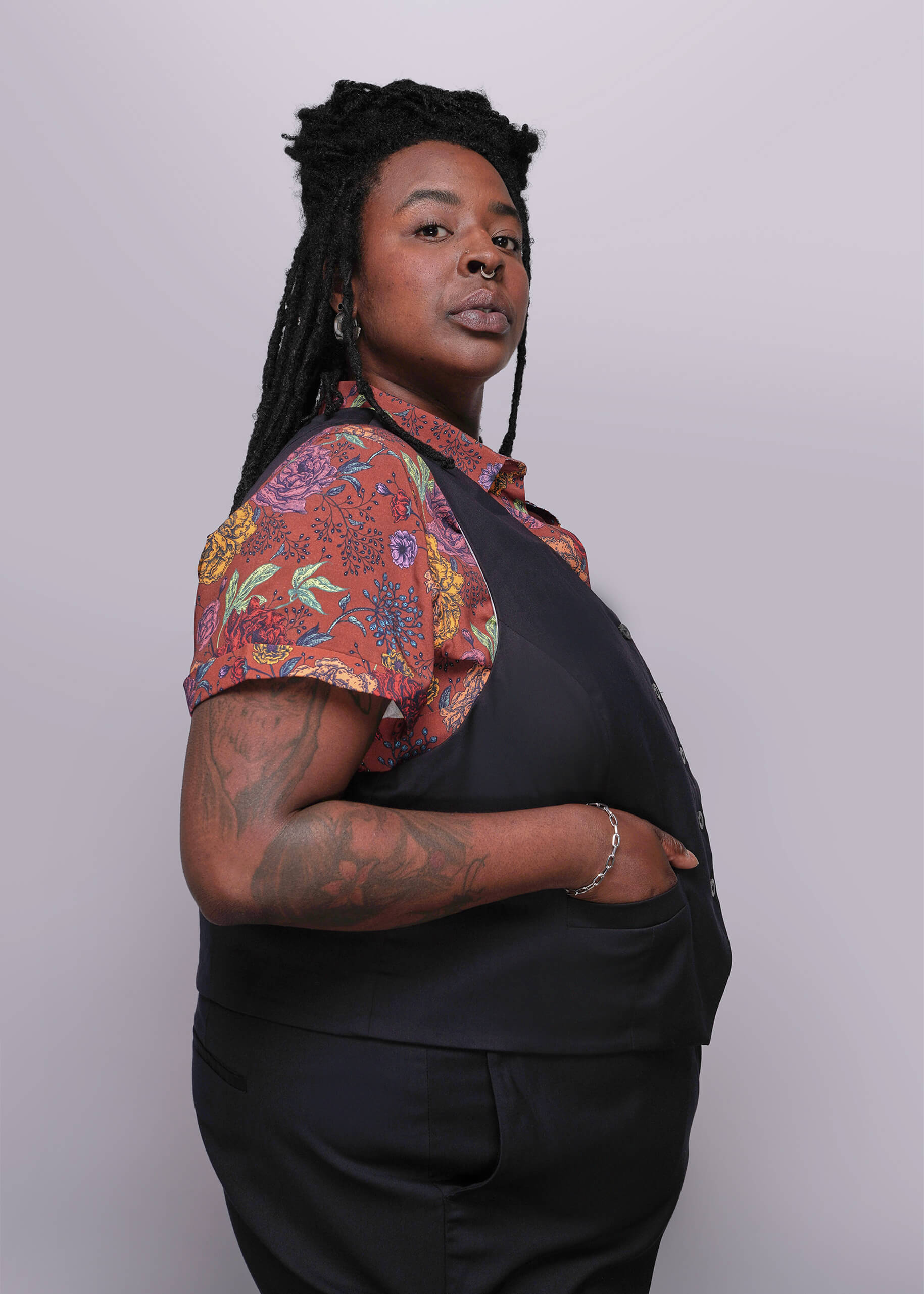 S=Person wearing a black outfit with a colorful floral shirt over the shoulders against a white background