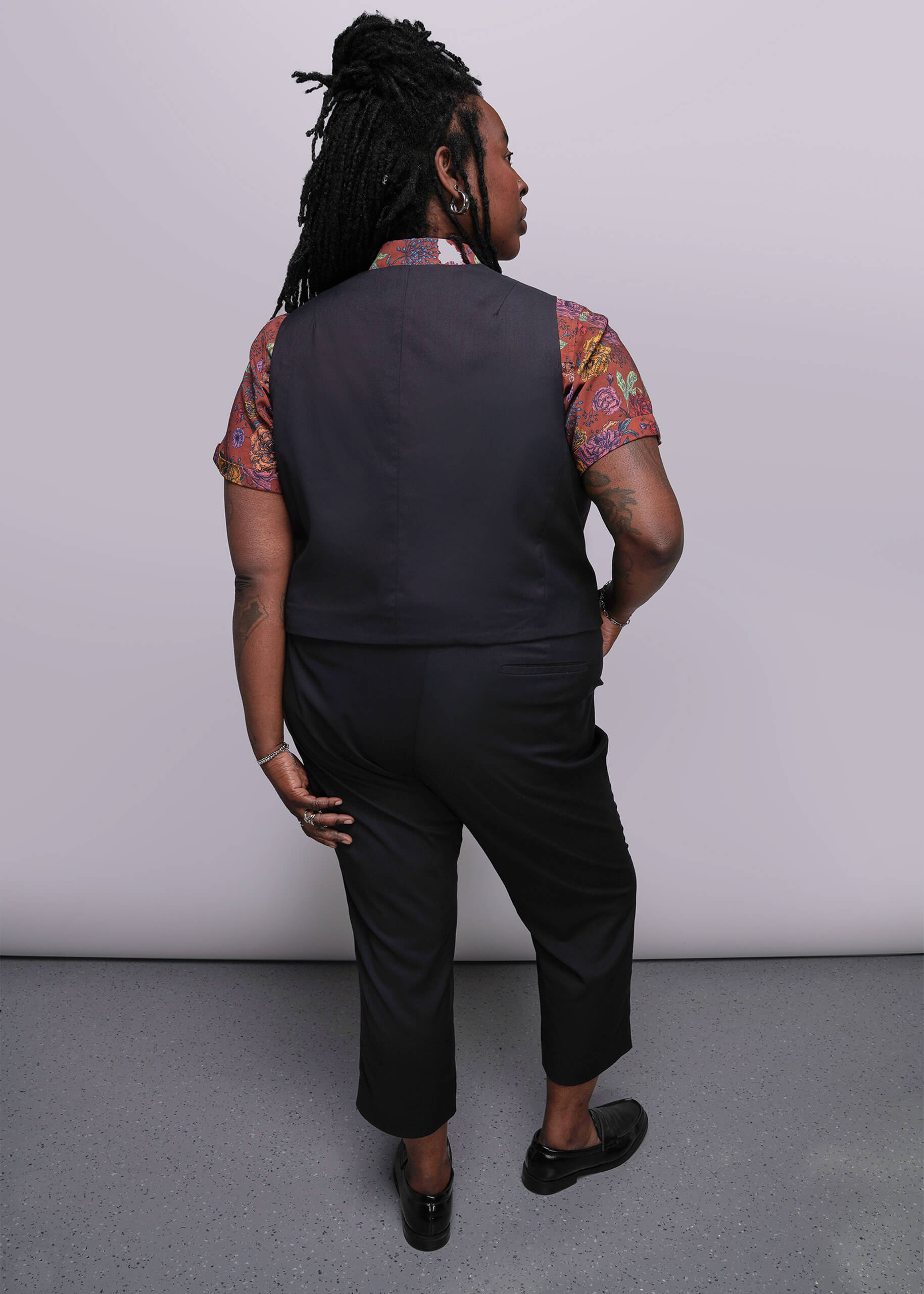 S=Person wearing a black vest and pants with a patterned shirt against a plain background
