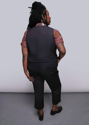 S=Person wearing a black vest and pants with a patterned shirt against a plain background