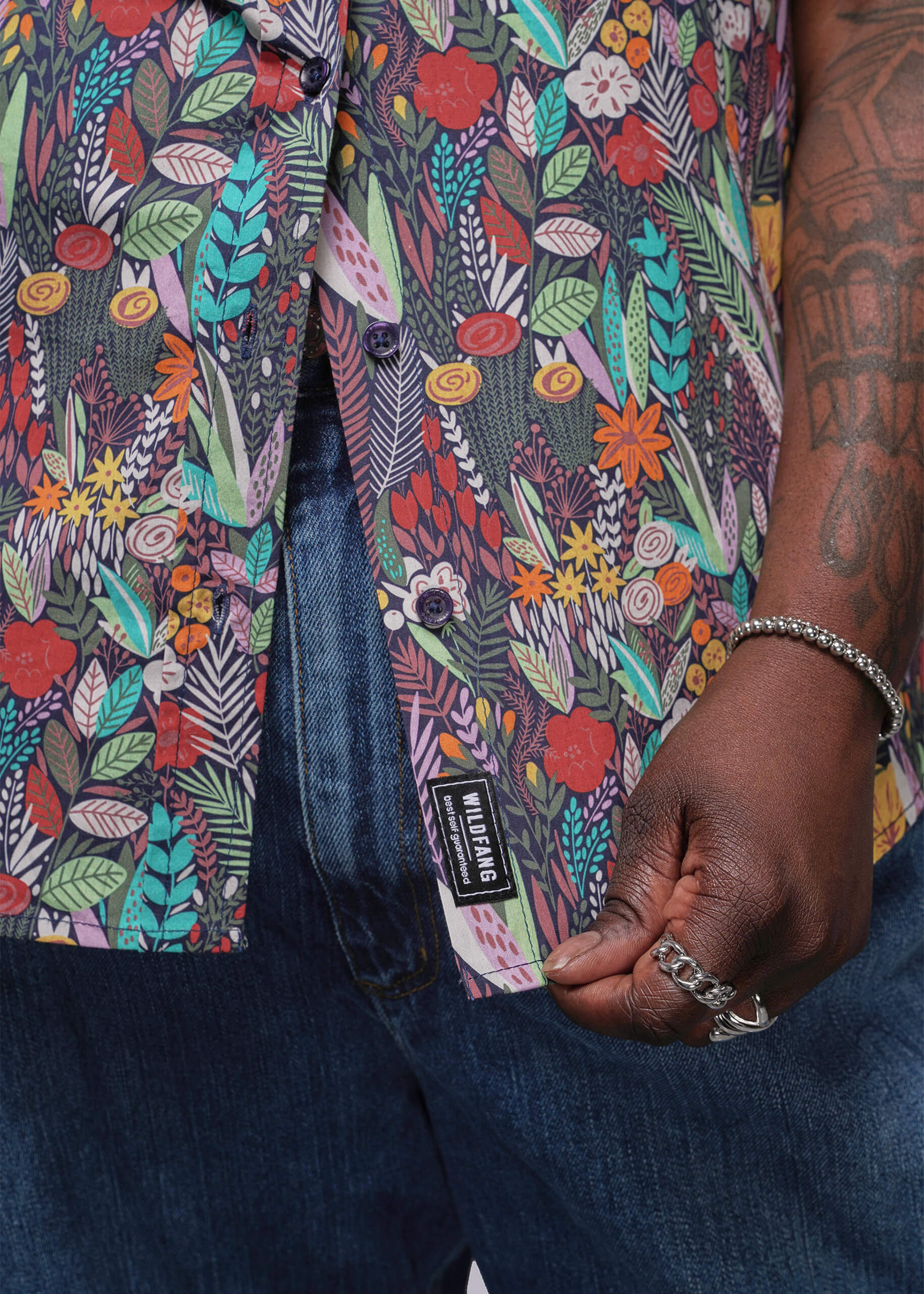 1X=Close-up of a colorful floral-patterned shirt with a brand label, worn by a person.