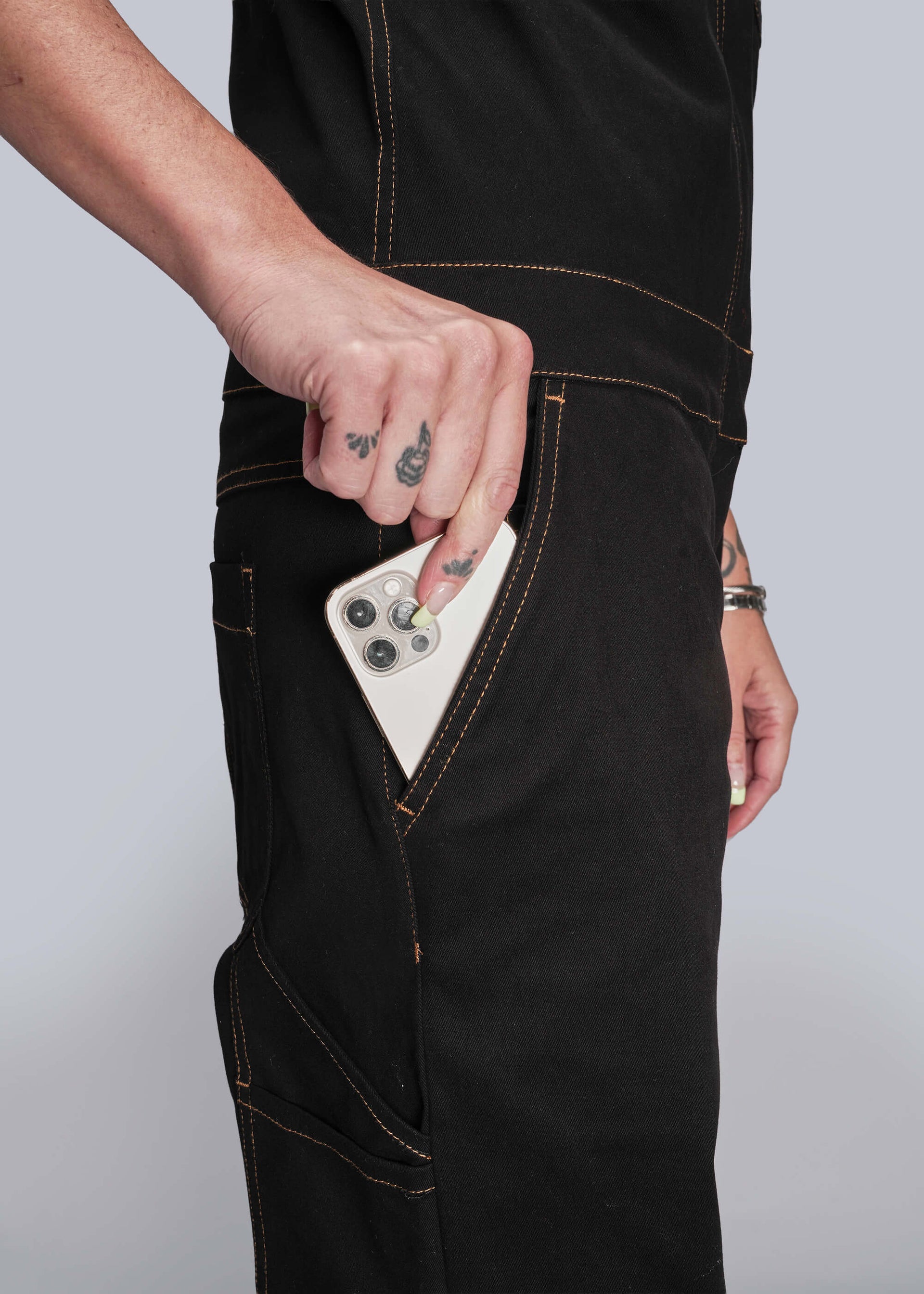 S=Person wearing black jeans with a white phone in the pocket against a light gray background