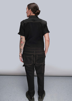 S=Person wearing a black jumpsuit against a plain background