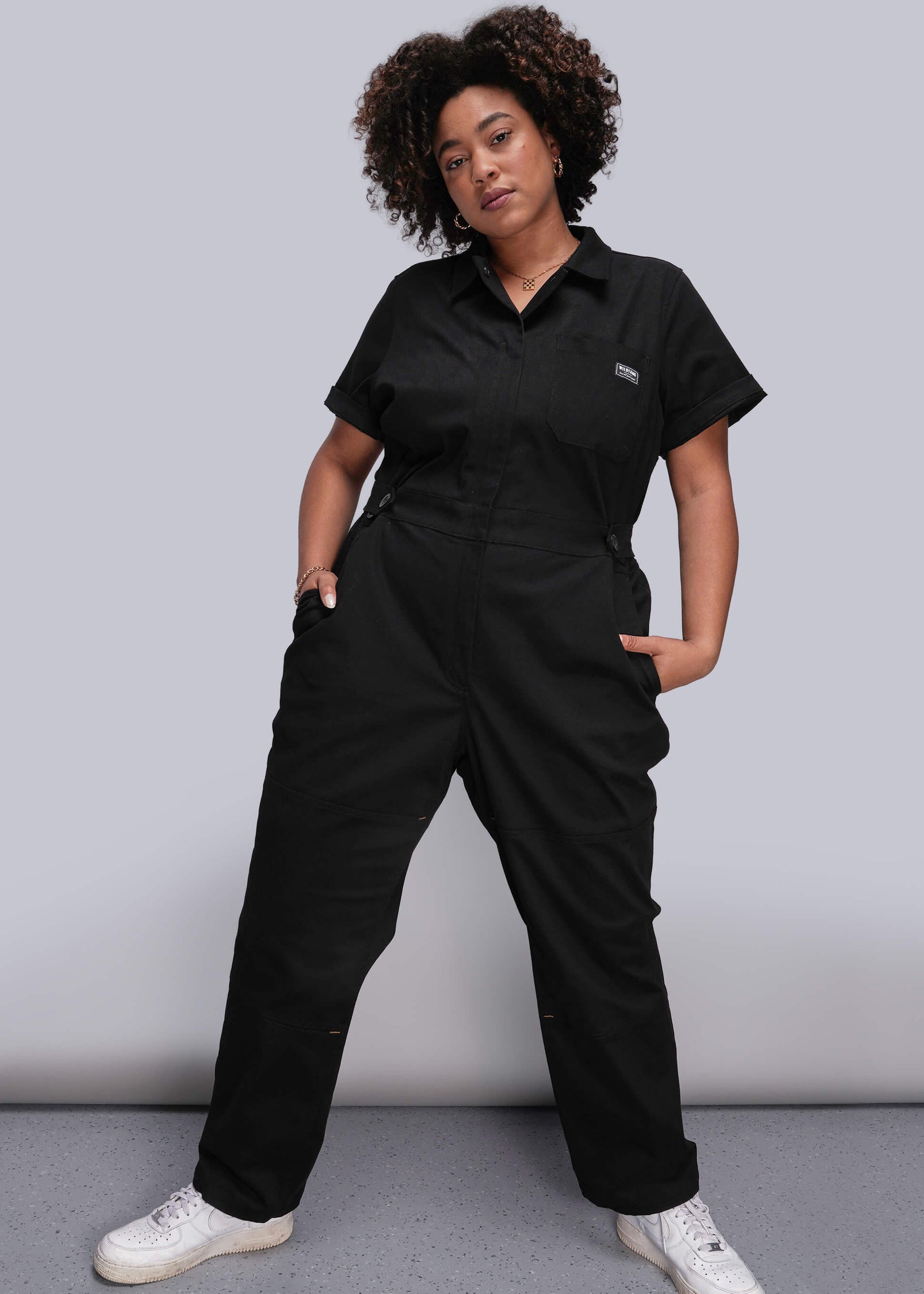 1X=Person wearing a black jumpsuit with a logo on a gray background