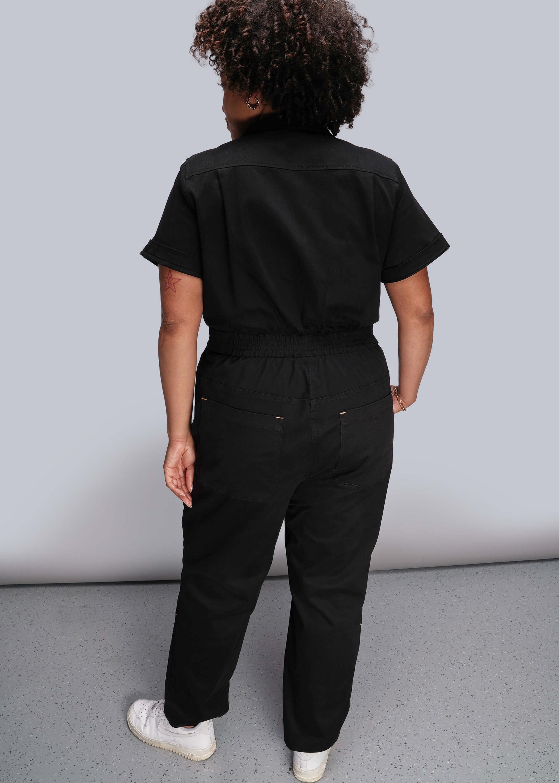 1X=Close up of person wearing a black coverall against a plain background