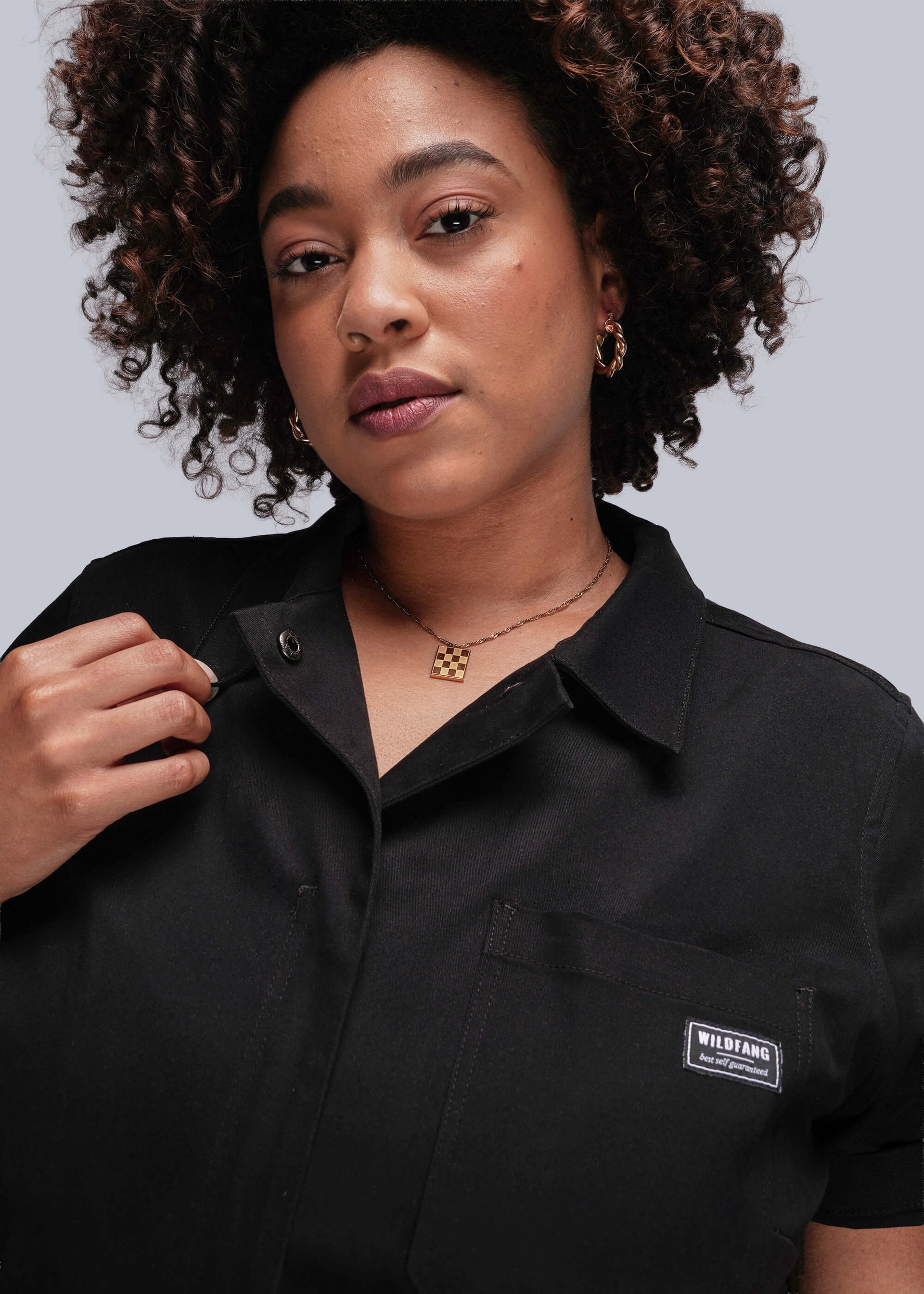 1X=Close up of person wearing a black coverall with a Wildfang logo on a gray background
