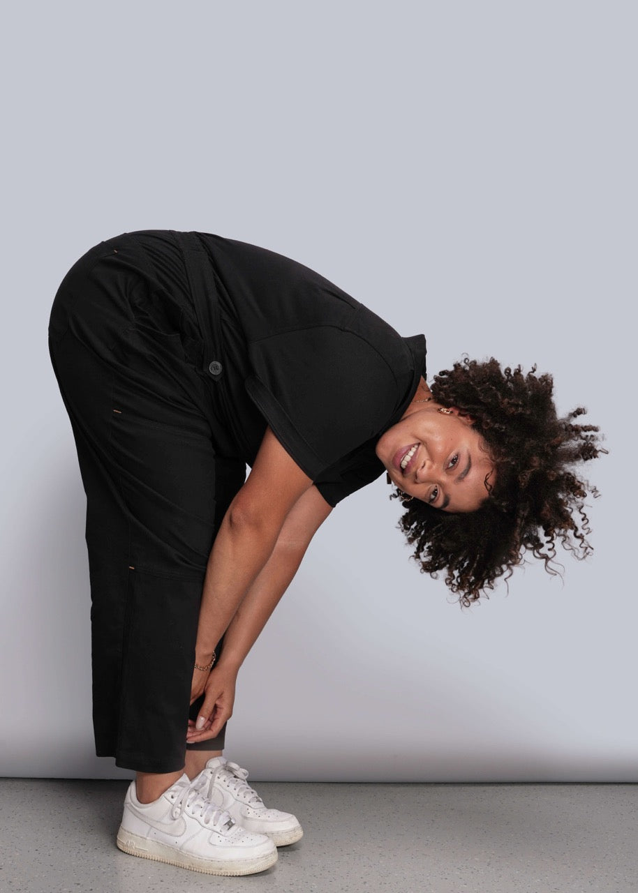 1X=Person wearing a black outfit and white sneakers against a plain background