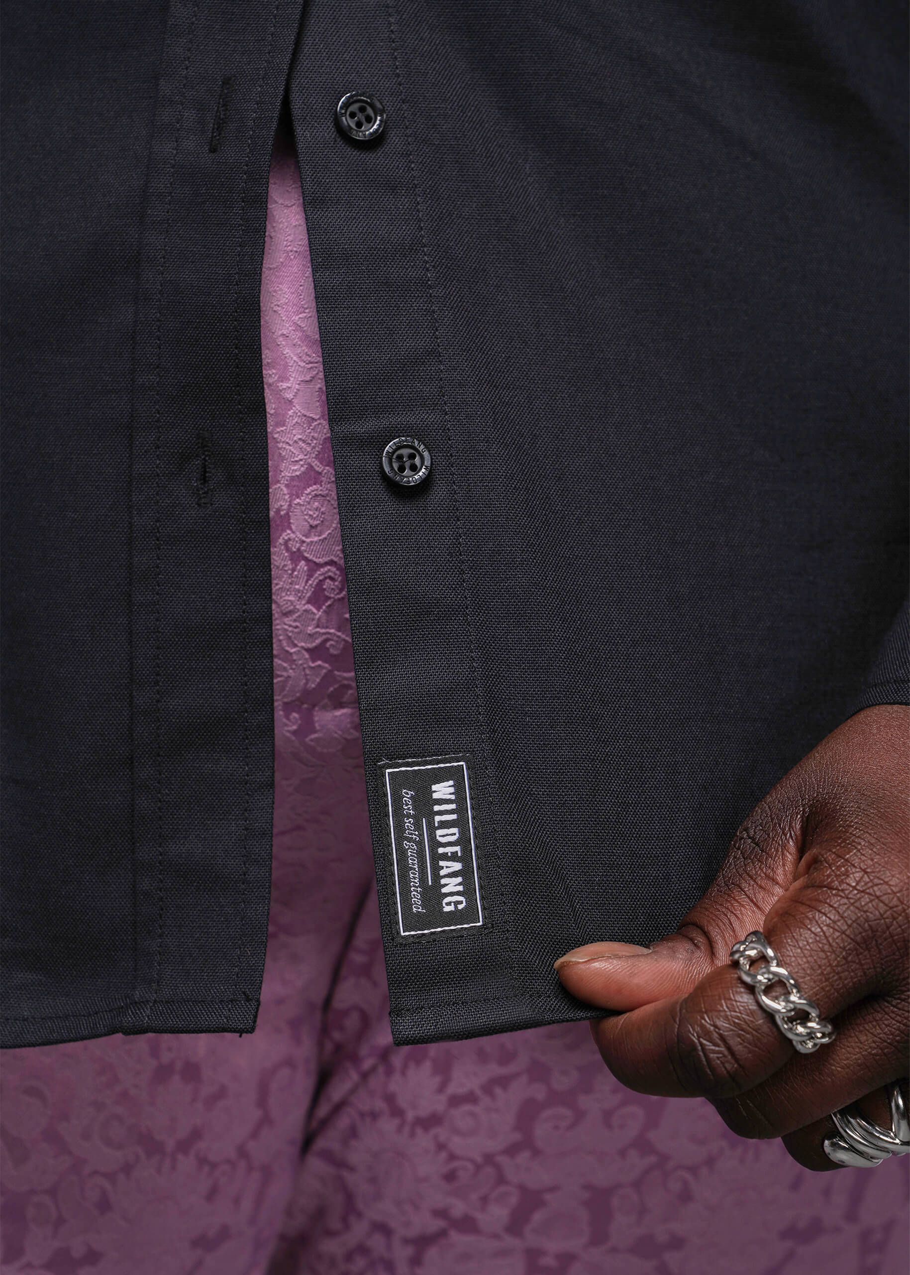 1X=Close-up of a black shirt with a brand label on a purple patterned background