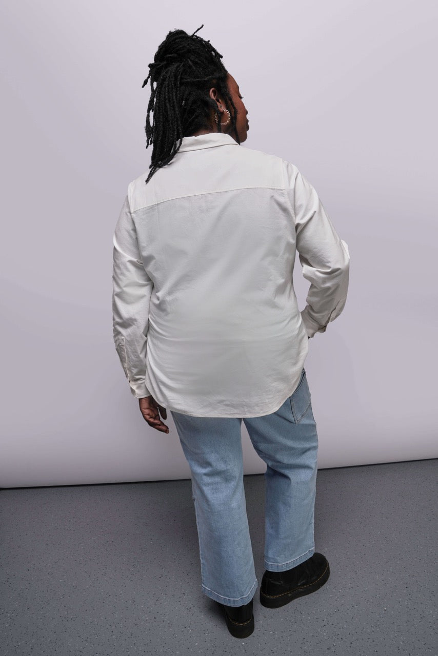 1X=Person wearing a light-colored shirt and jeans from behind on a plain background