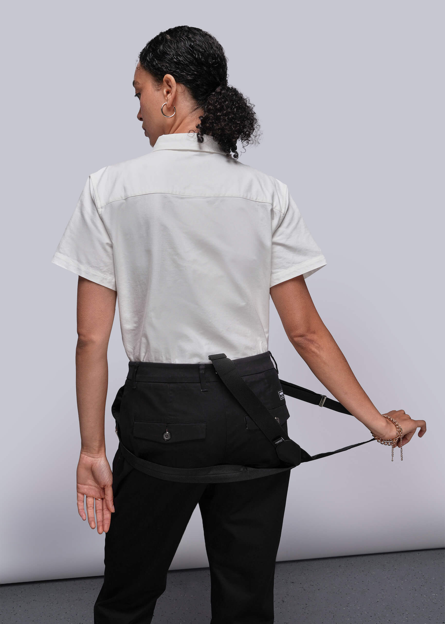 S=Person wearing a white shirt and black apron against a plain background