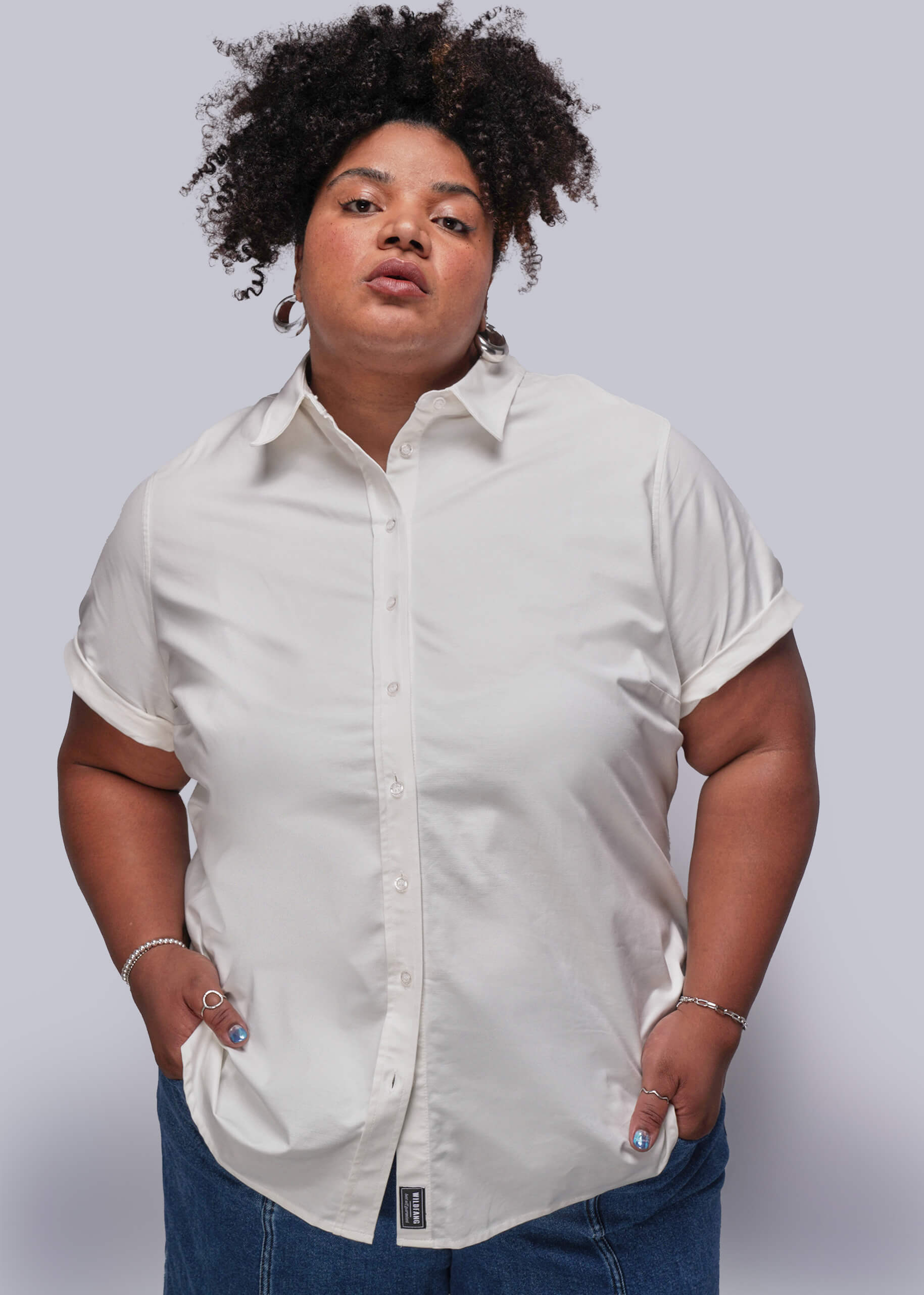 1X=Person wearing a light-colored button-up shirt and jeans against a plain background