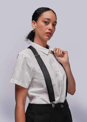 S=Person wearing a white shirt and black suspenders against a light gray background