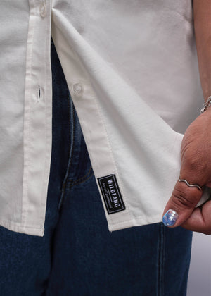 1X=Close-up of a person wearing a white shirt with a brand label on the chest pocket.
