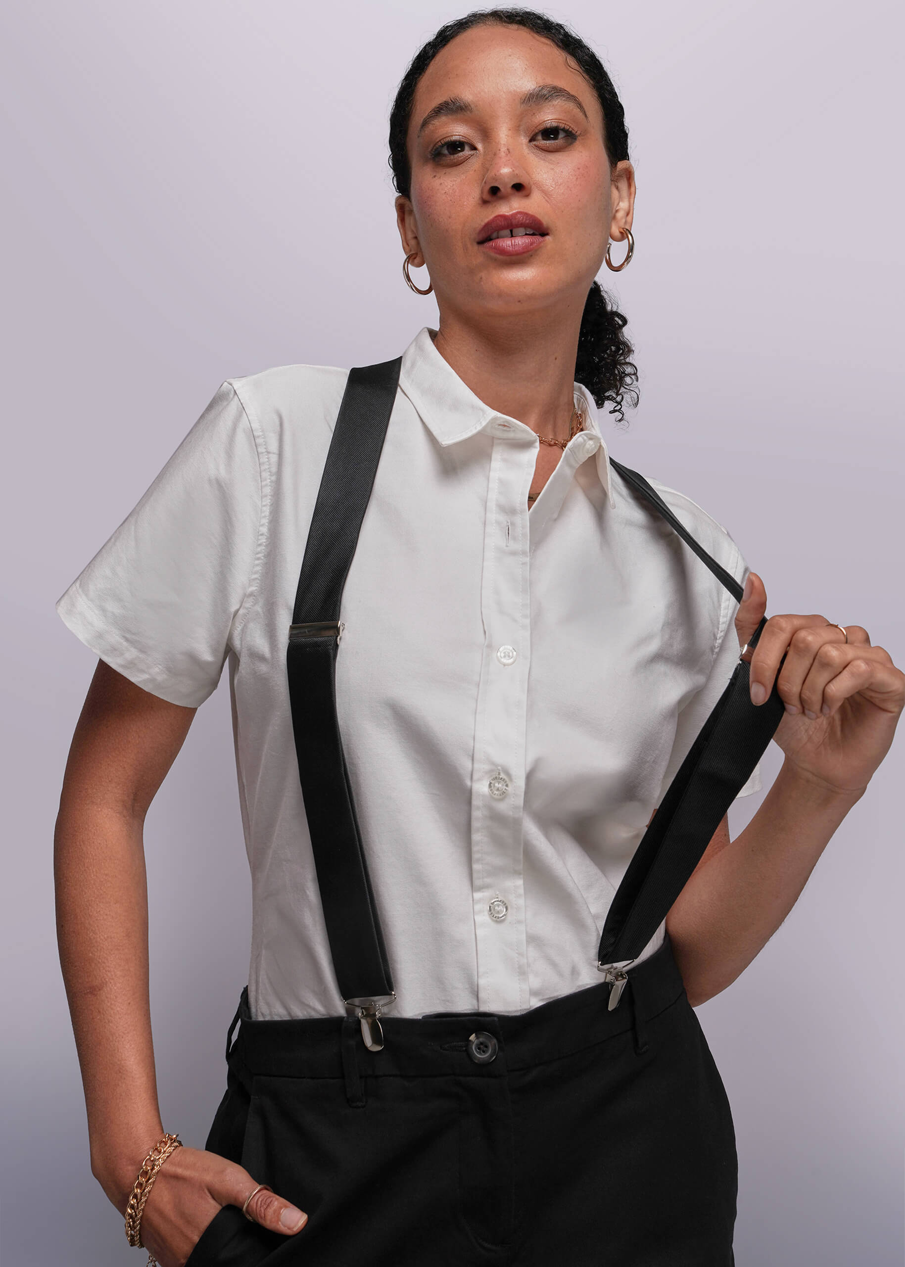 Person wearing a white shirt with black suspenders against a plain background