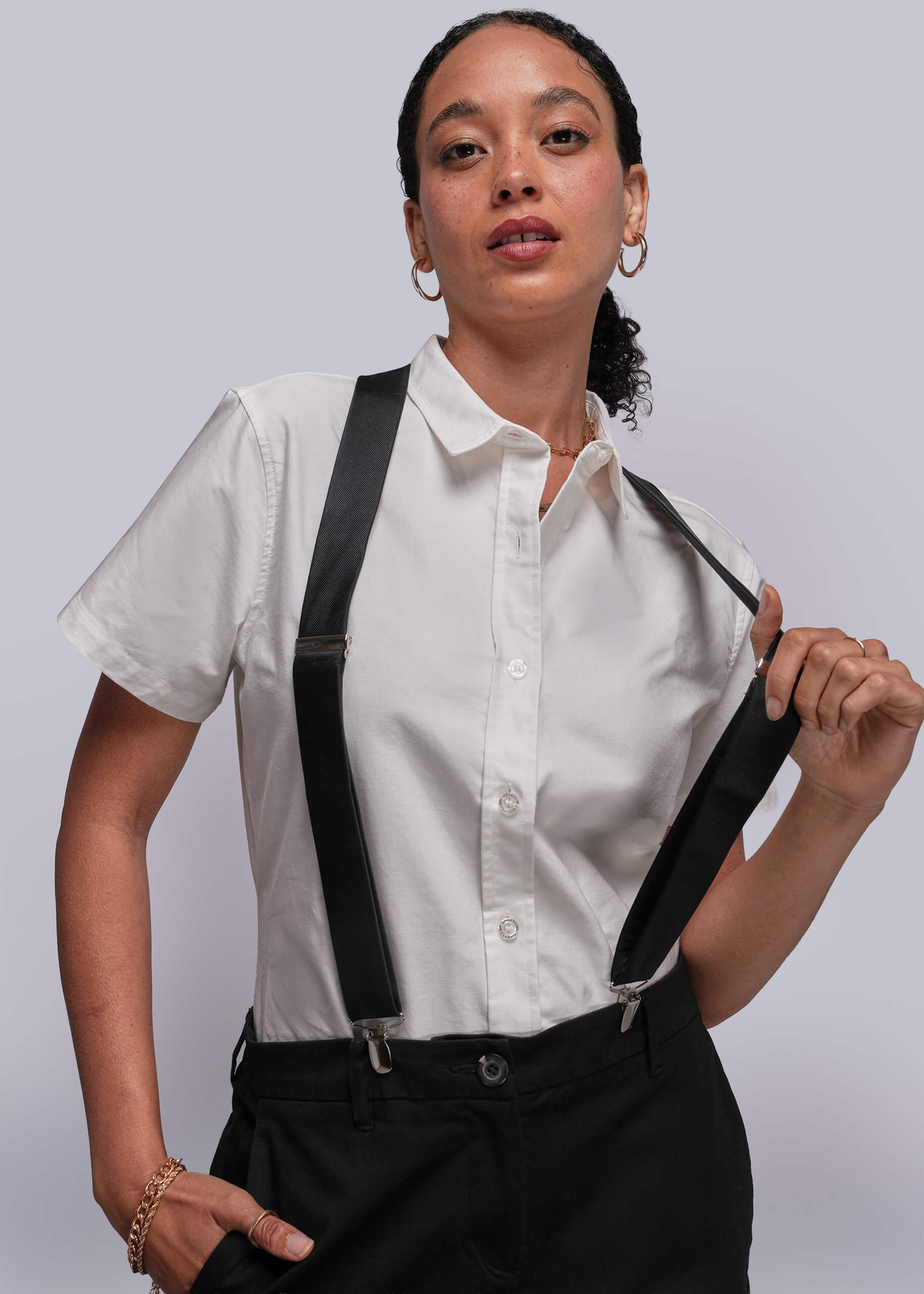S=Person wearing a white shirt with black suspenders against a plain background