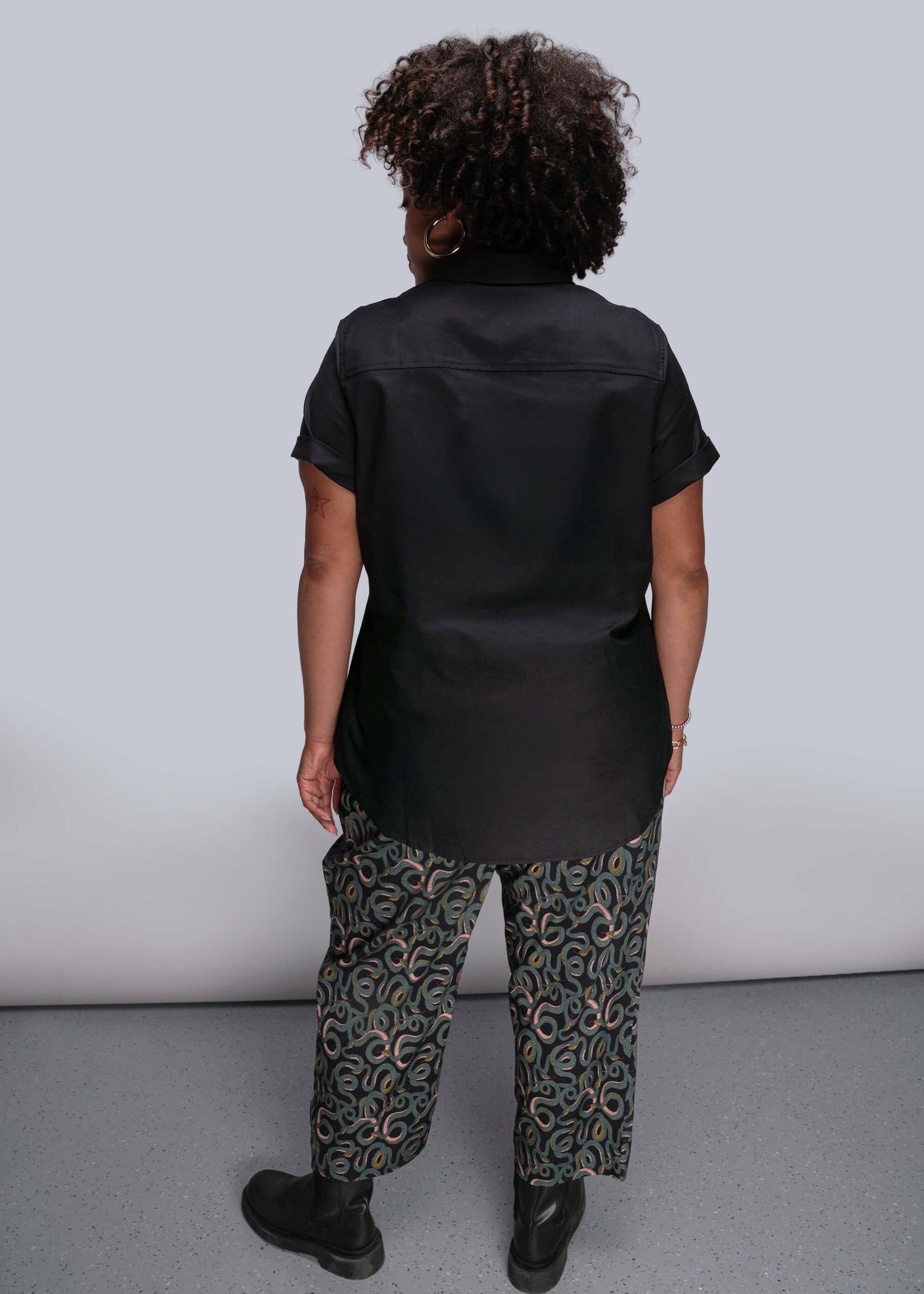 1X=Person wearing a black shirt and patterned pants against a plain background