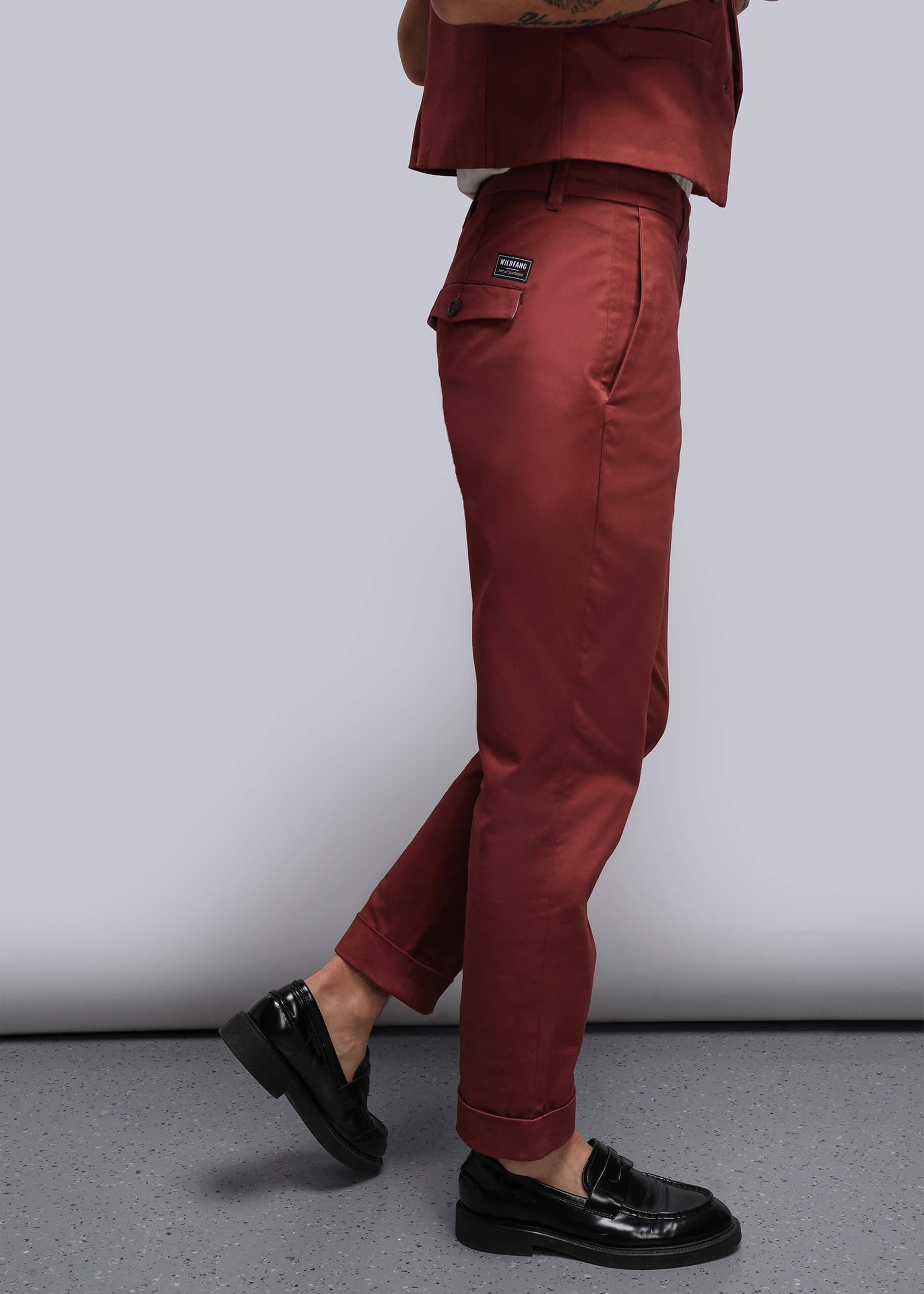 S=Person wearing reddish orange pants and black shoes on a plain background