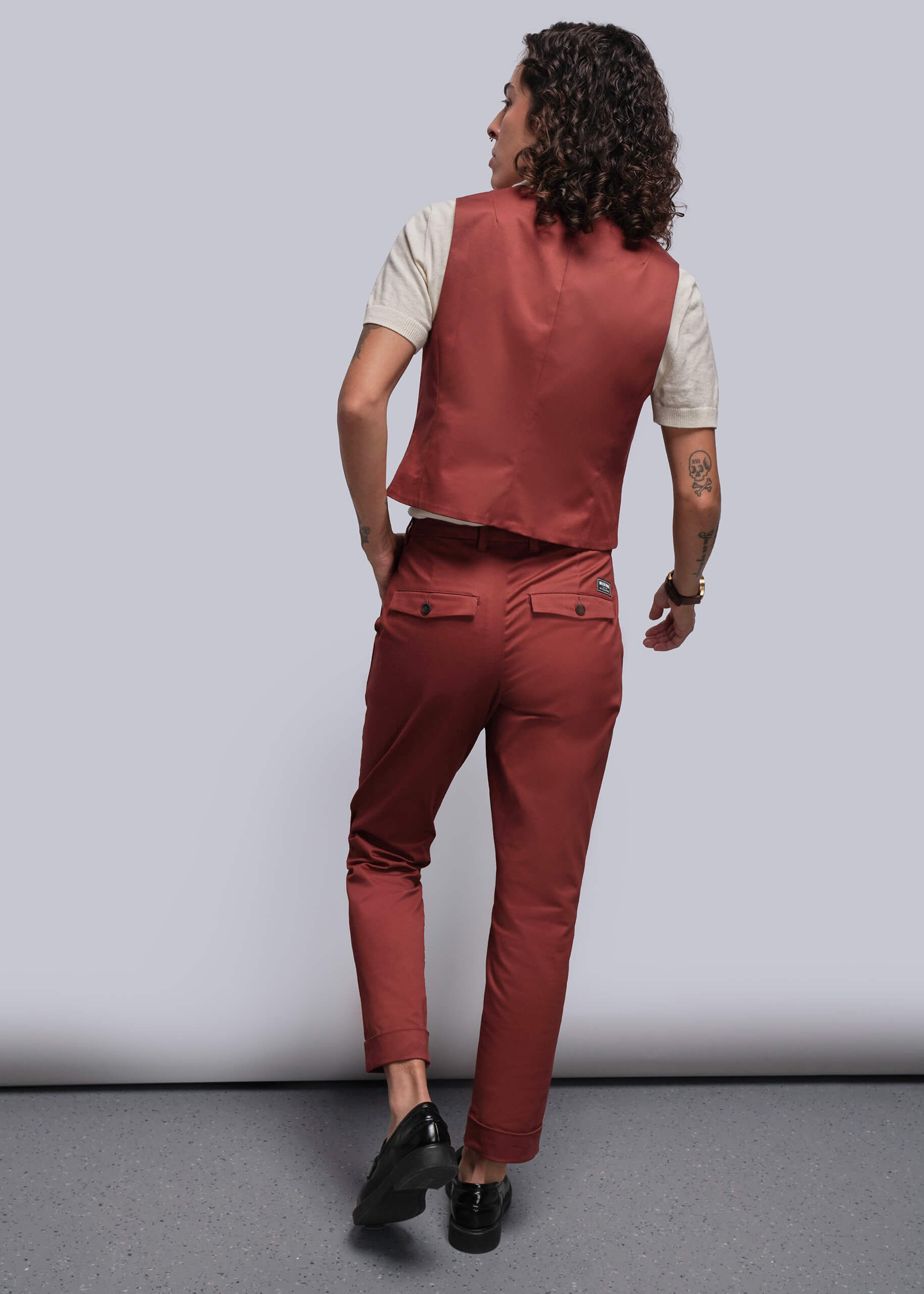 S=Person wearing a reddish orange colored vest and pants against a gray background