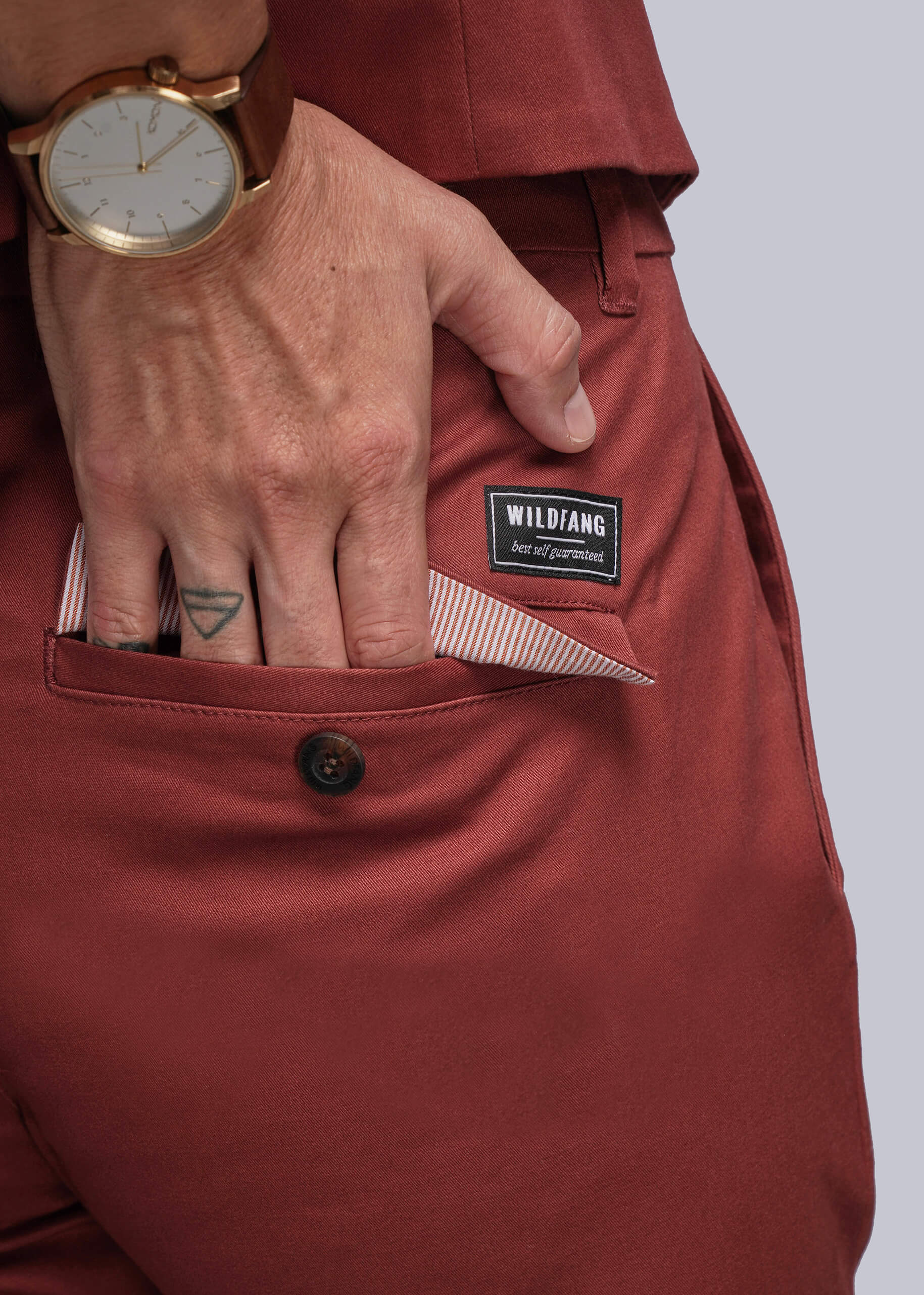 S=Close up of person putting hand in back pocket of reddish orange colored pants
