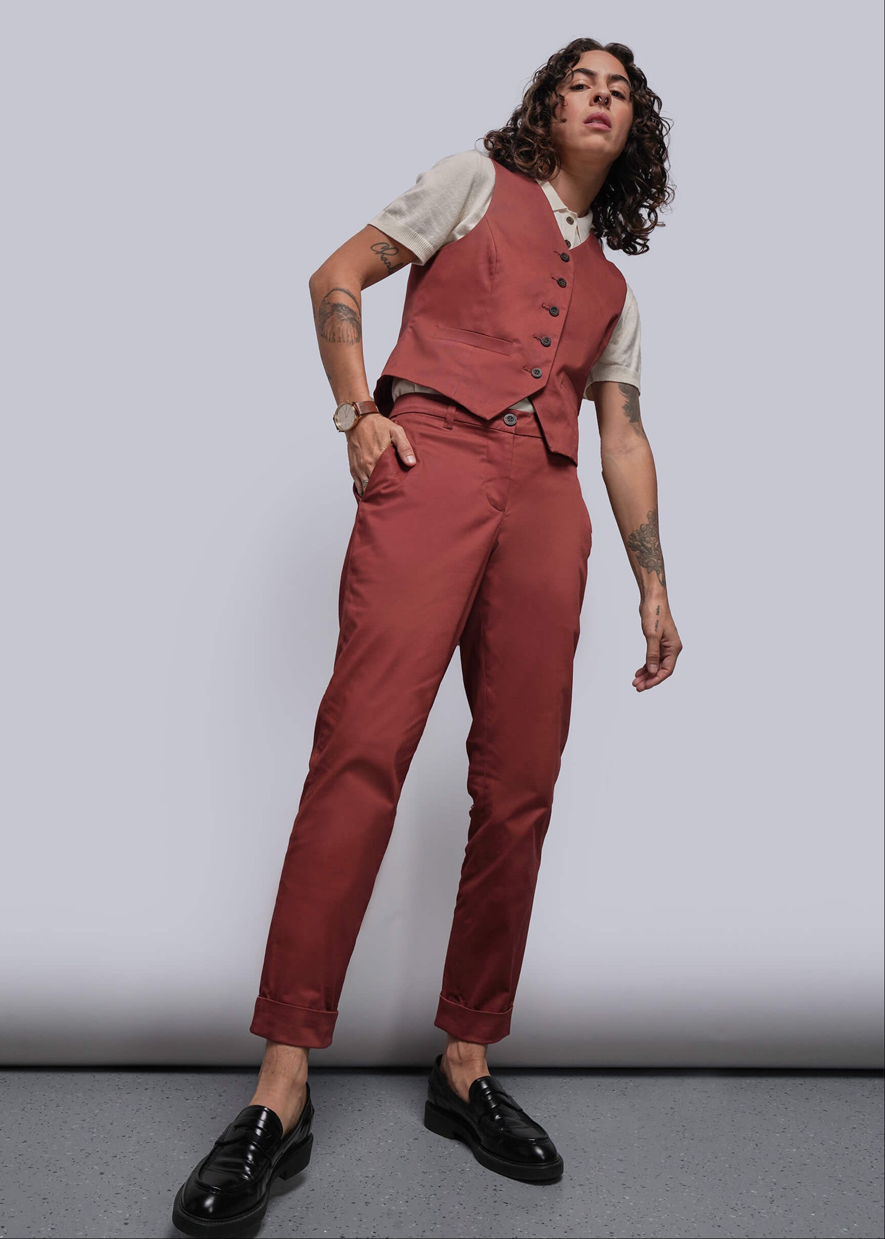 S=Person wearing a rust colored vest and pants with an off white polo sweater underneath on a plain background