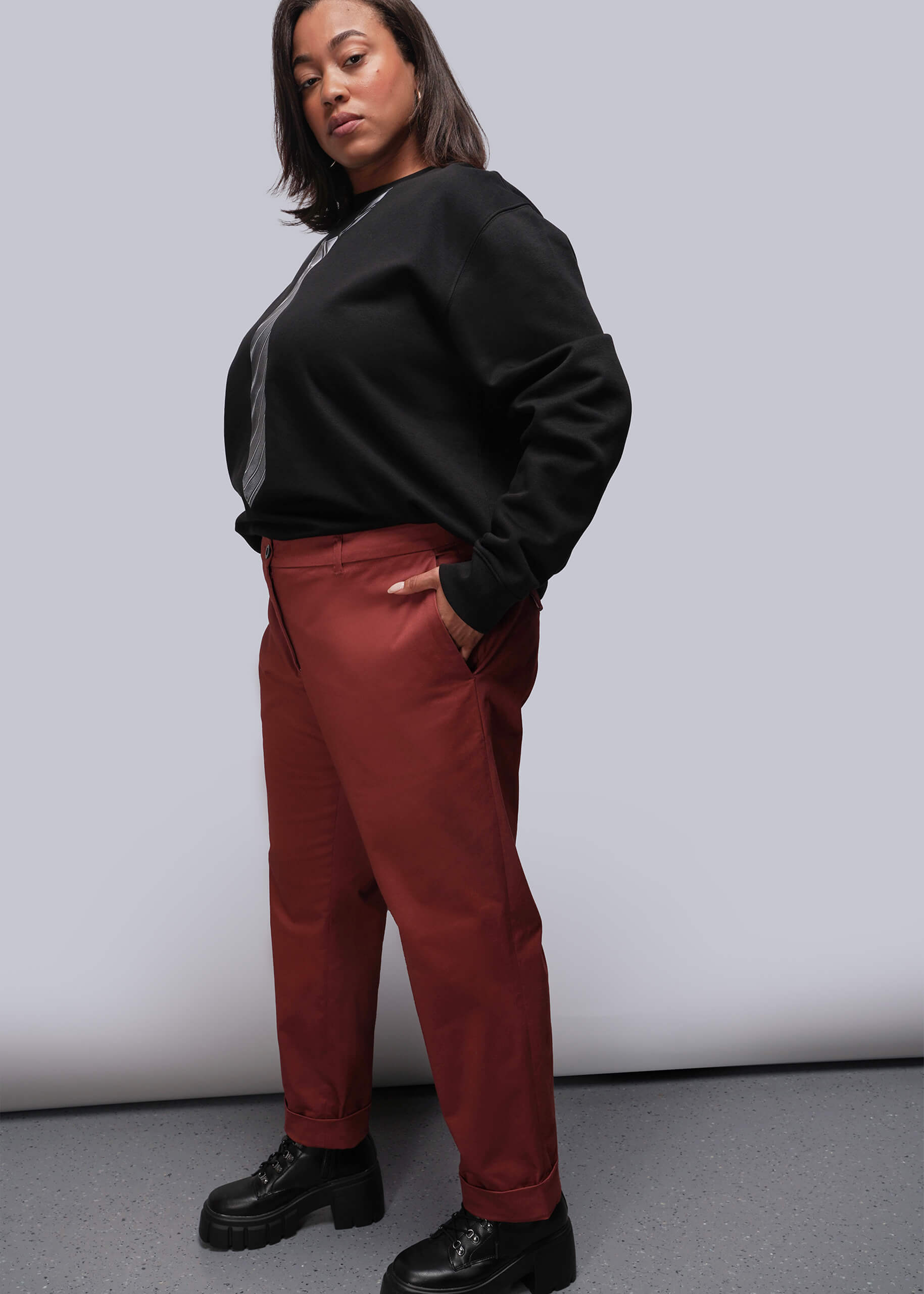 1X=Person wearing a black sweater and red orange pants against a plain background