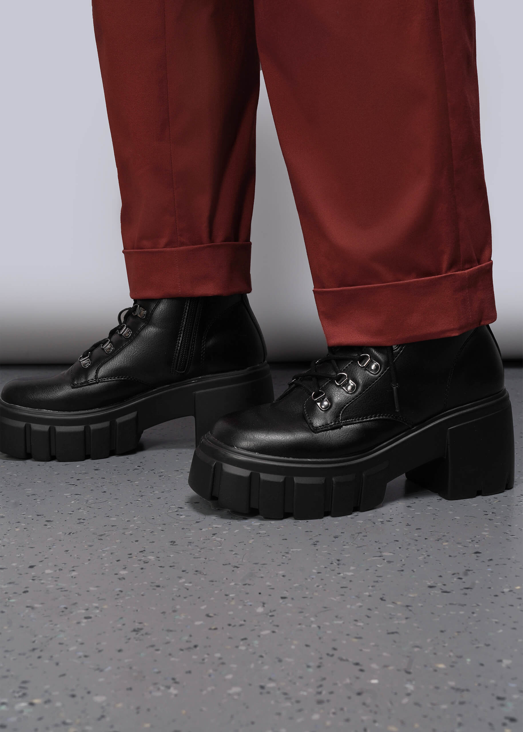 1X=Black platform shoes worn with red  orange pants on a gray floor.