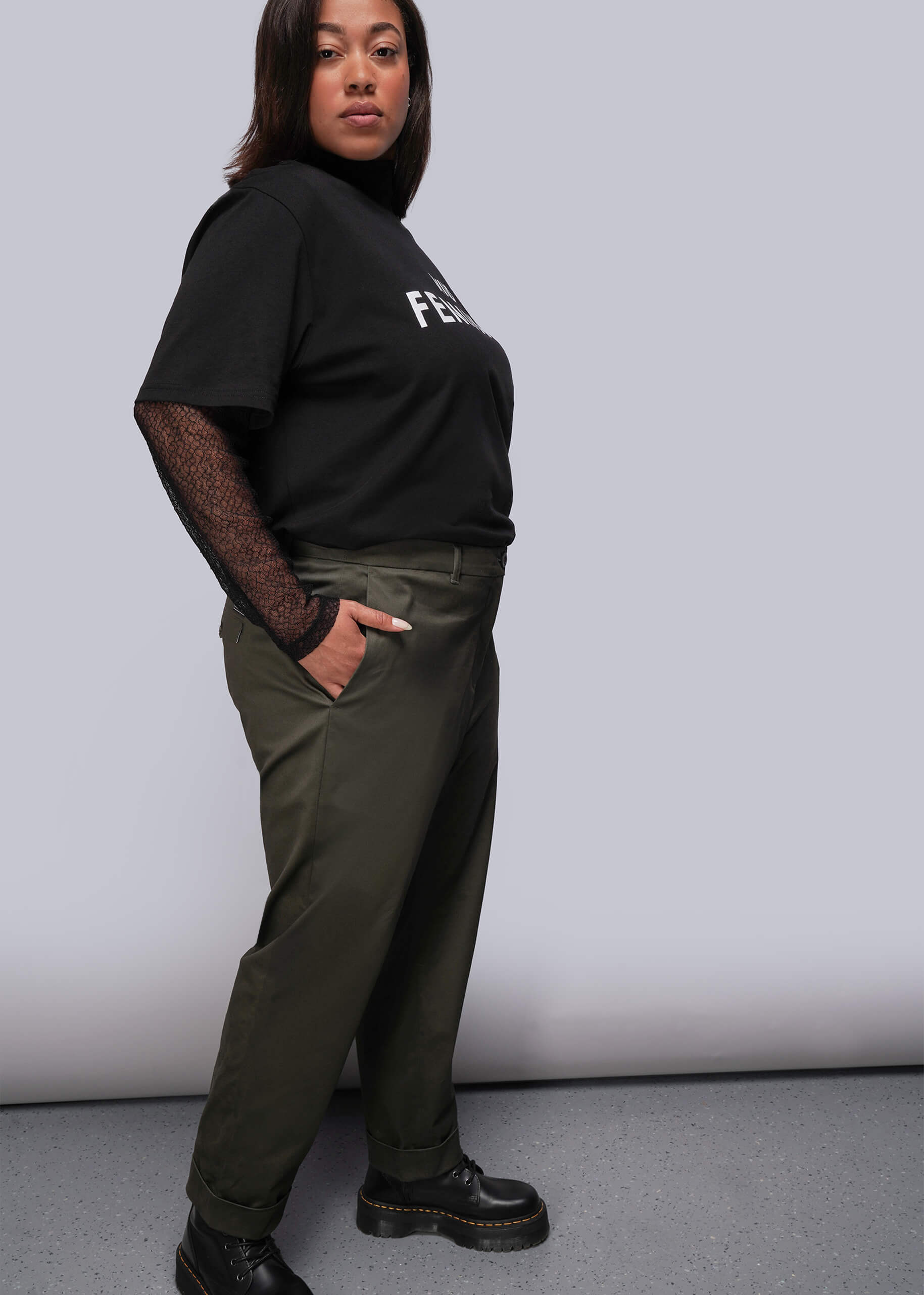 1X=Person wearing a black t-shirt with text and green pants against a plain background
