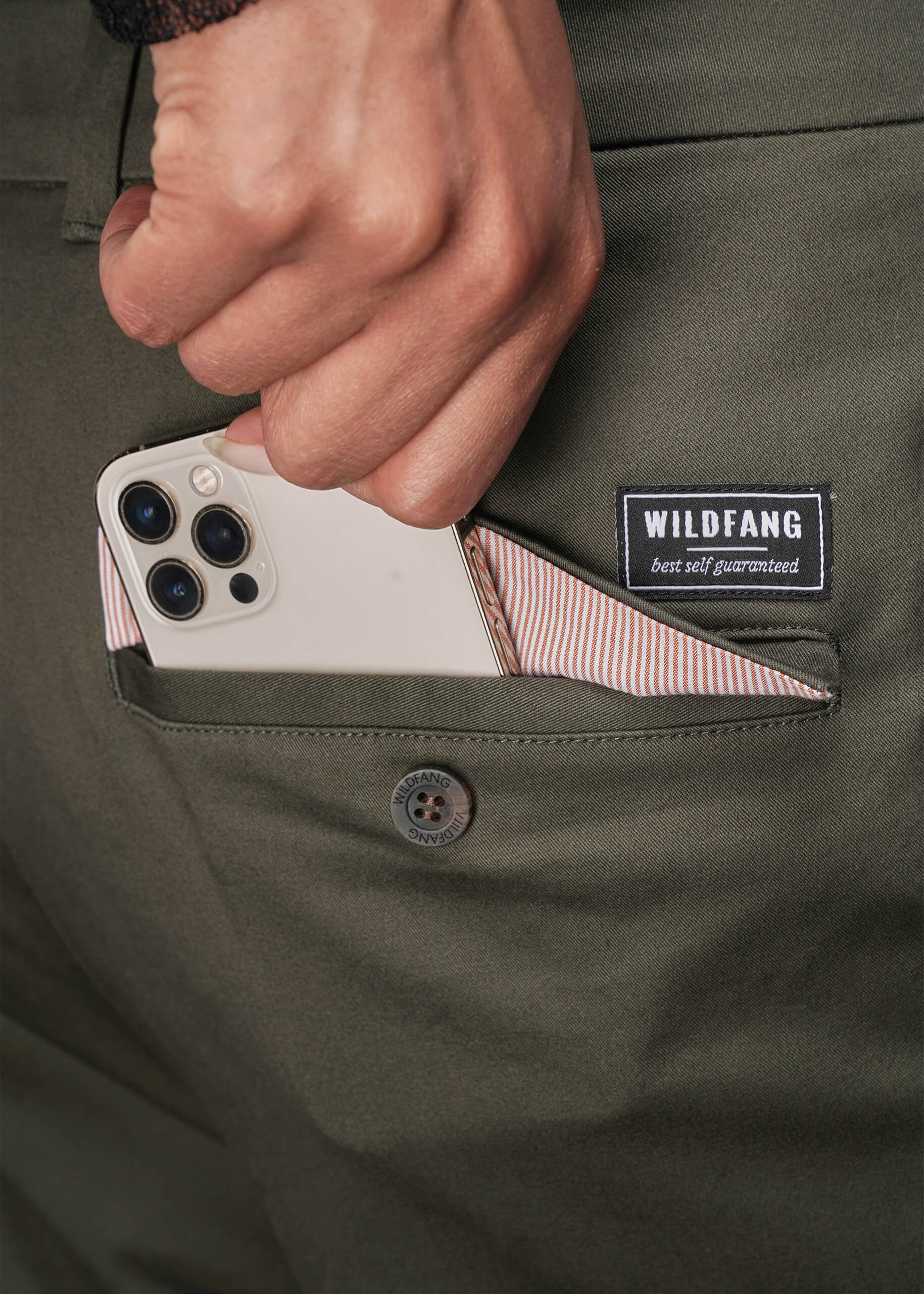 1X=Person holding a phone in a pocket of green pants with a Wildfang label.