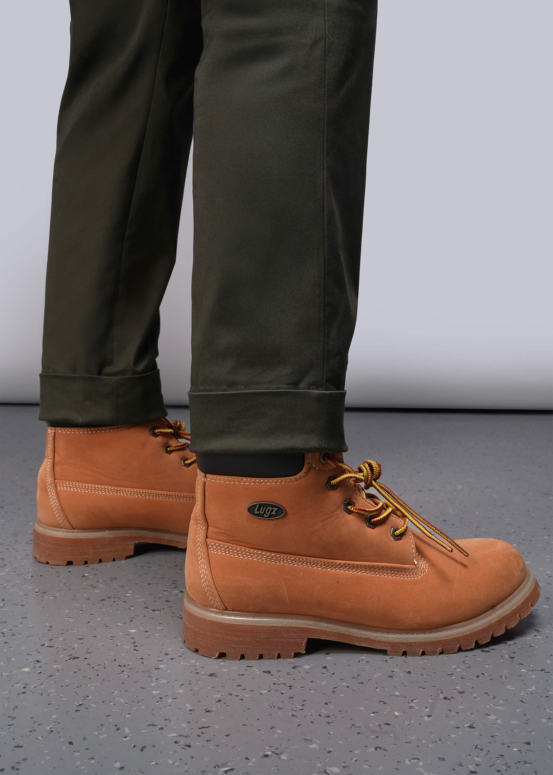S=Brown boots worn with olive pants on a gray floor.