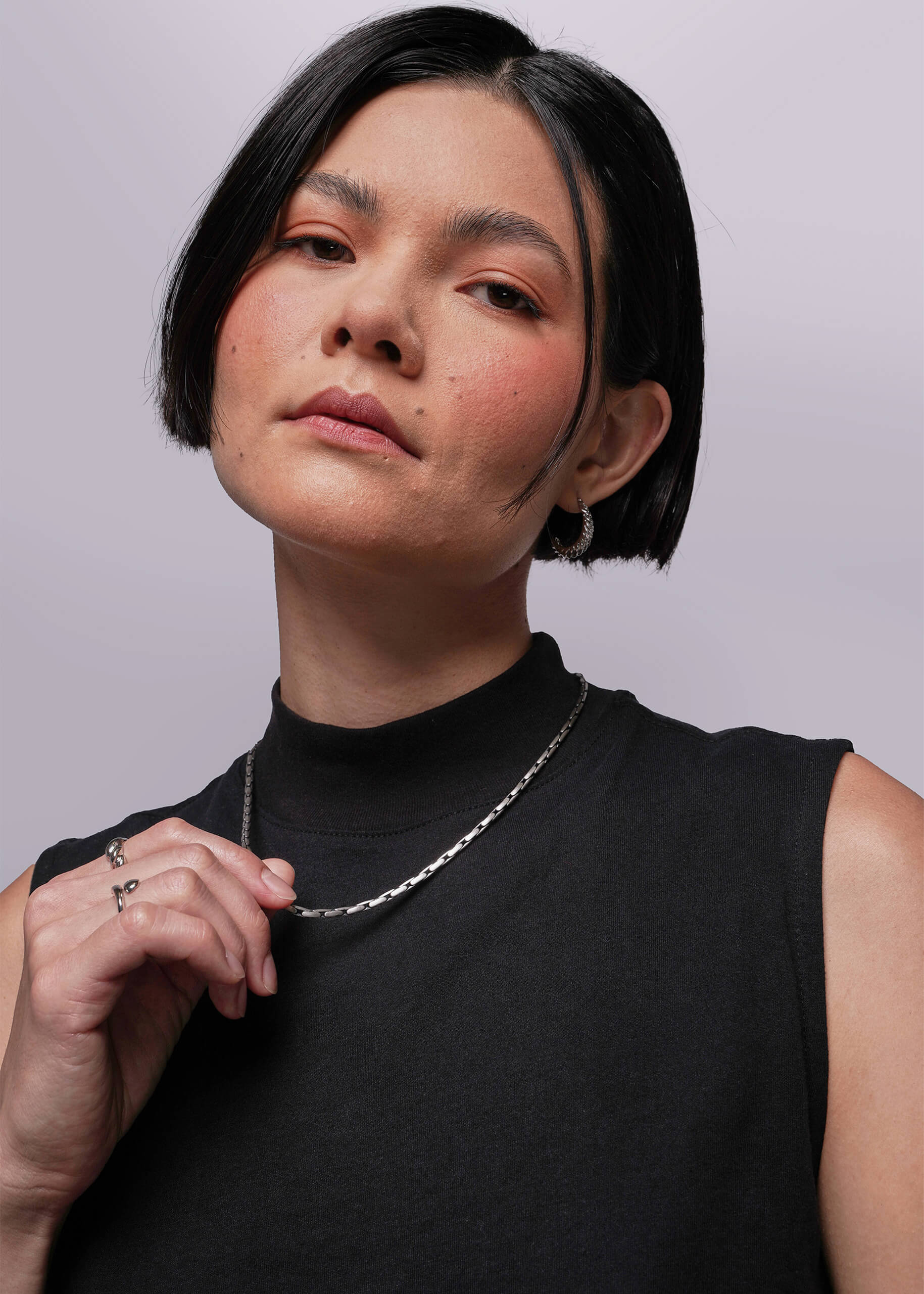 S=Person wearing a black sleeveless top and silver necklace against a light gray background