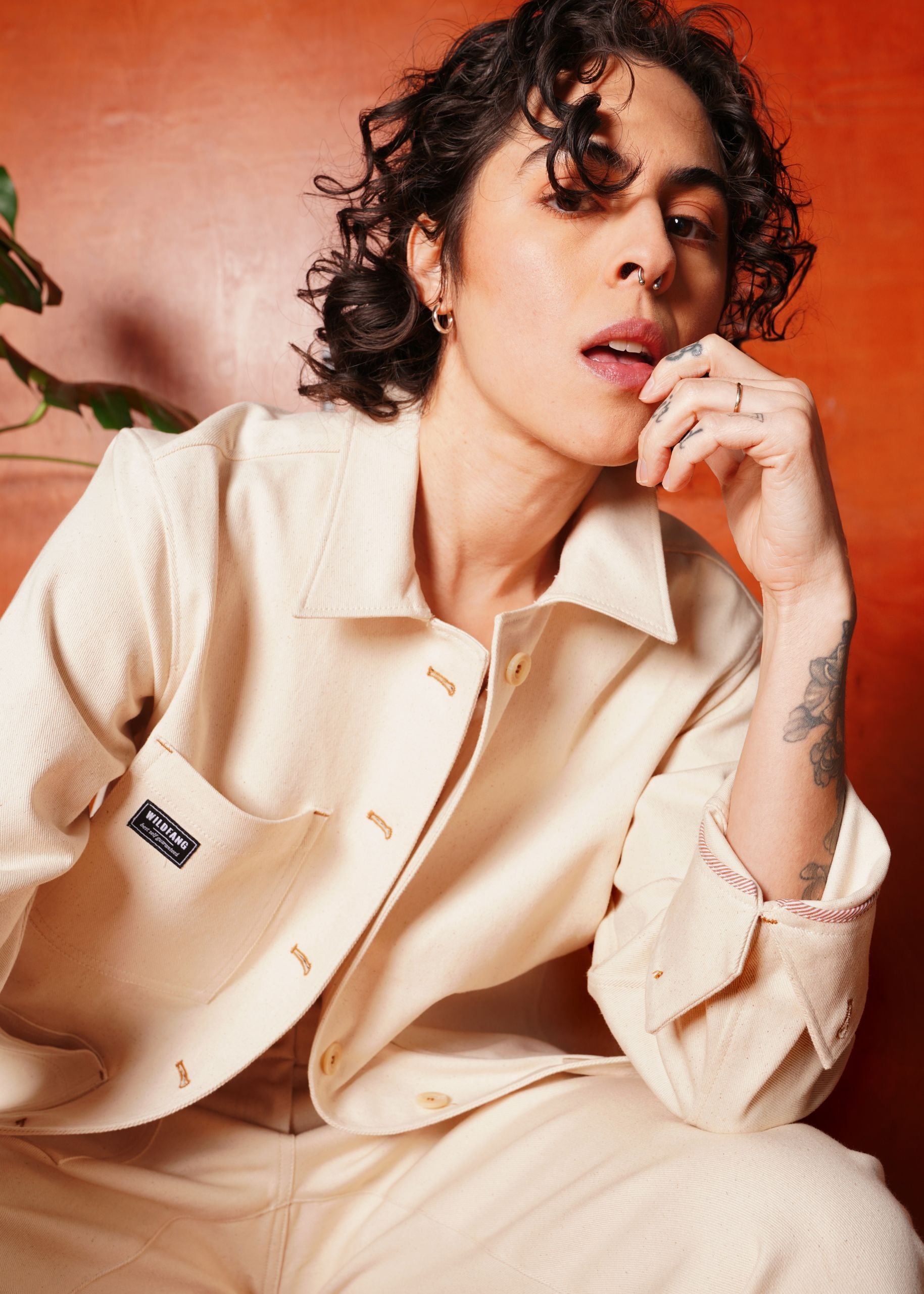 Person wearing a beige colored denim jacket with a Wildfang brand logo patch against an orange background