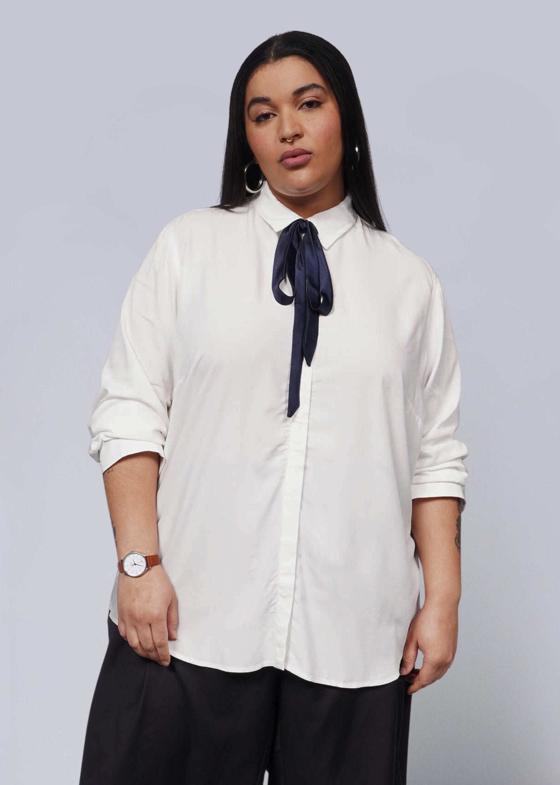 1X=Person wearing a white shirt with a navy bow and black pants on a light gray background